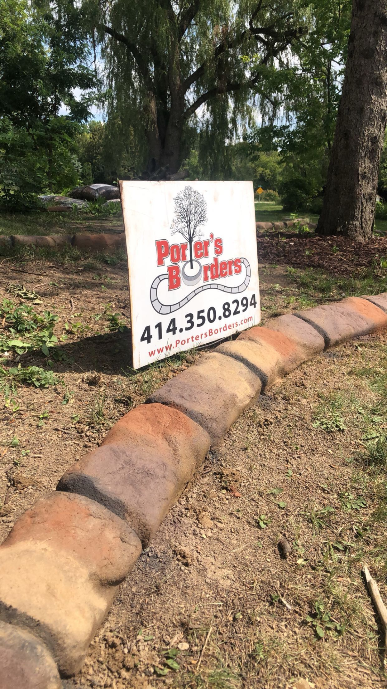A sign is sitting on top of a brick curb in a yard.