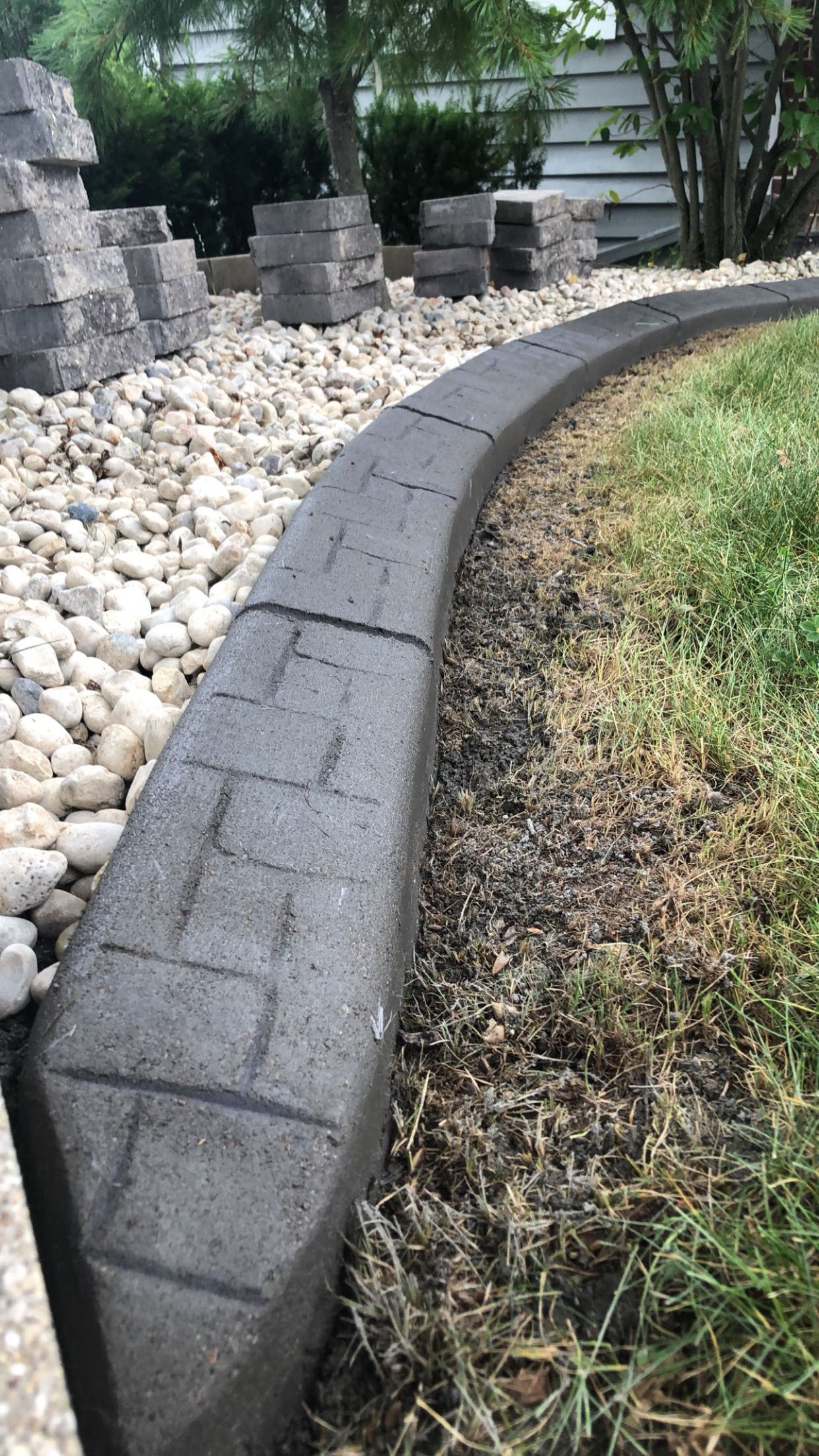 A concrete curb is surrounded by rocks and grass in a yard.