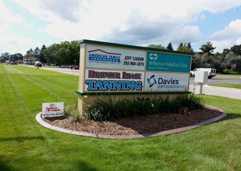 A sign for a tanning salon is in the middle of a lush green field