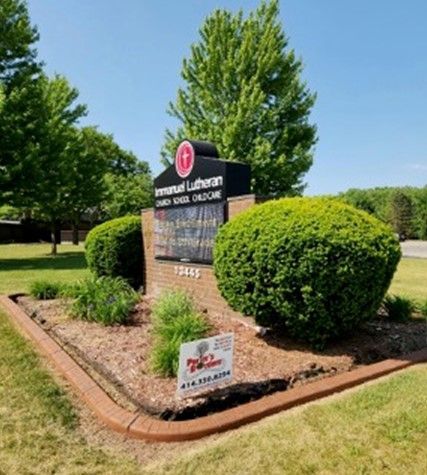 A sign for Emmanuel Lutheran church is surrounded by bushes and trees