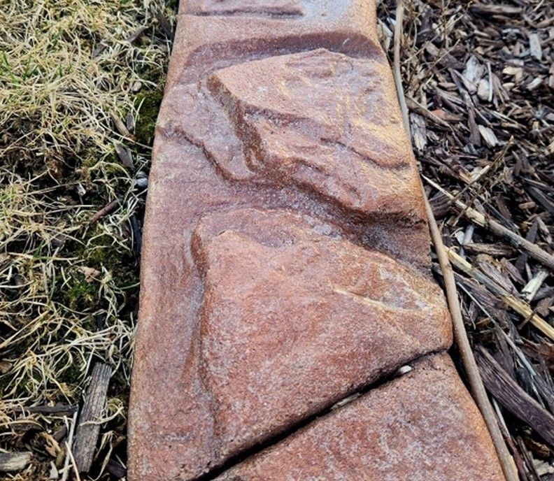 A large rock is sitting in the grass next to a pile of mulch