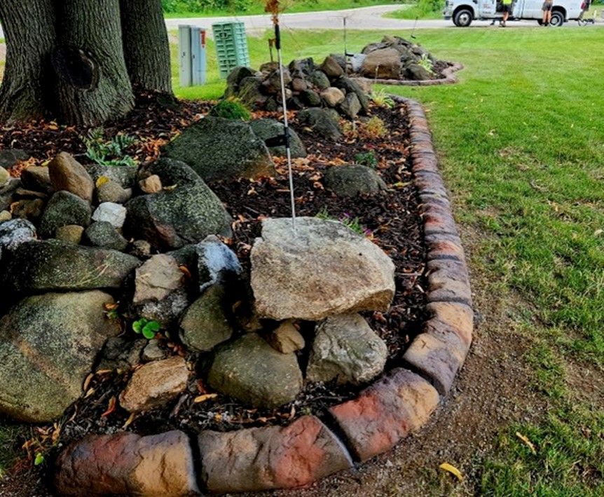 A rock garden with a brick border and a tree in the background