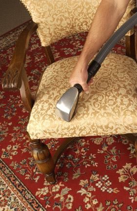 A person is cleaning a chair with a vacuum cleaner.