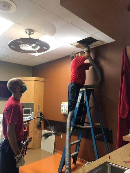A man on a ladder is vacuuming a hole in the ceiling