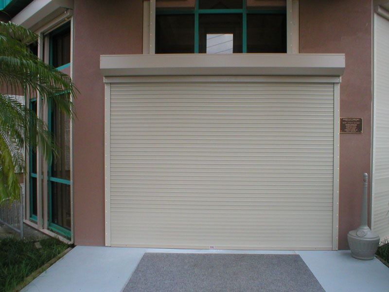 Closed beige roll-up garage door on a pink stucco building with a small potted plant nearby