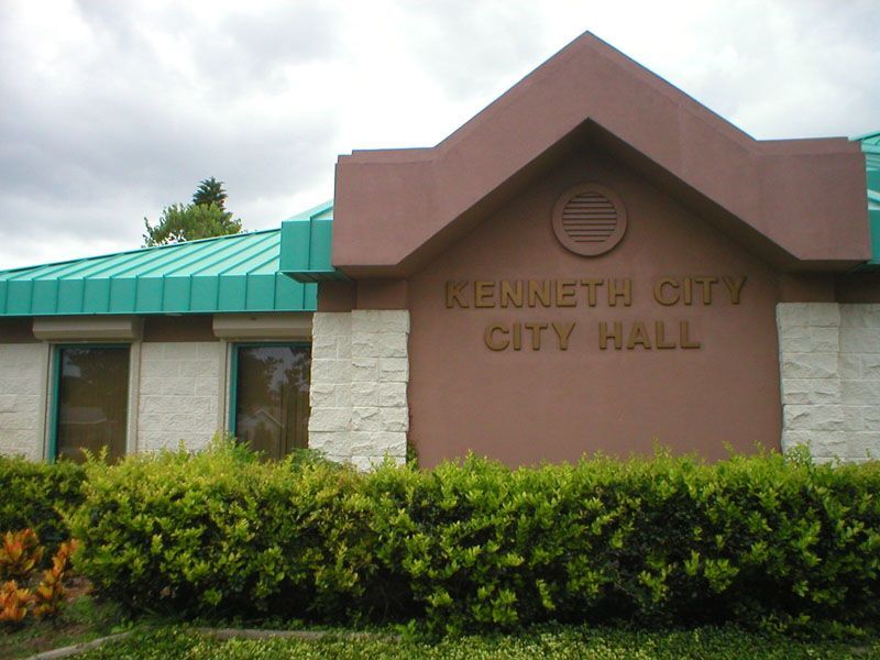 Kennett City Hall sign on a tan building with a green roof and shrubs in front