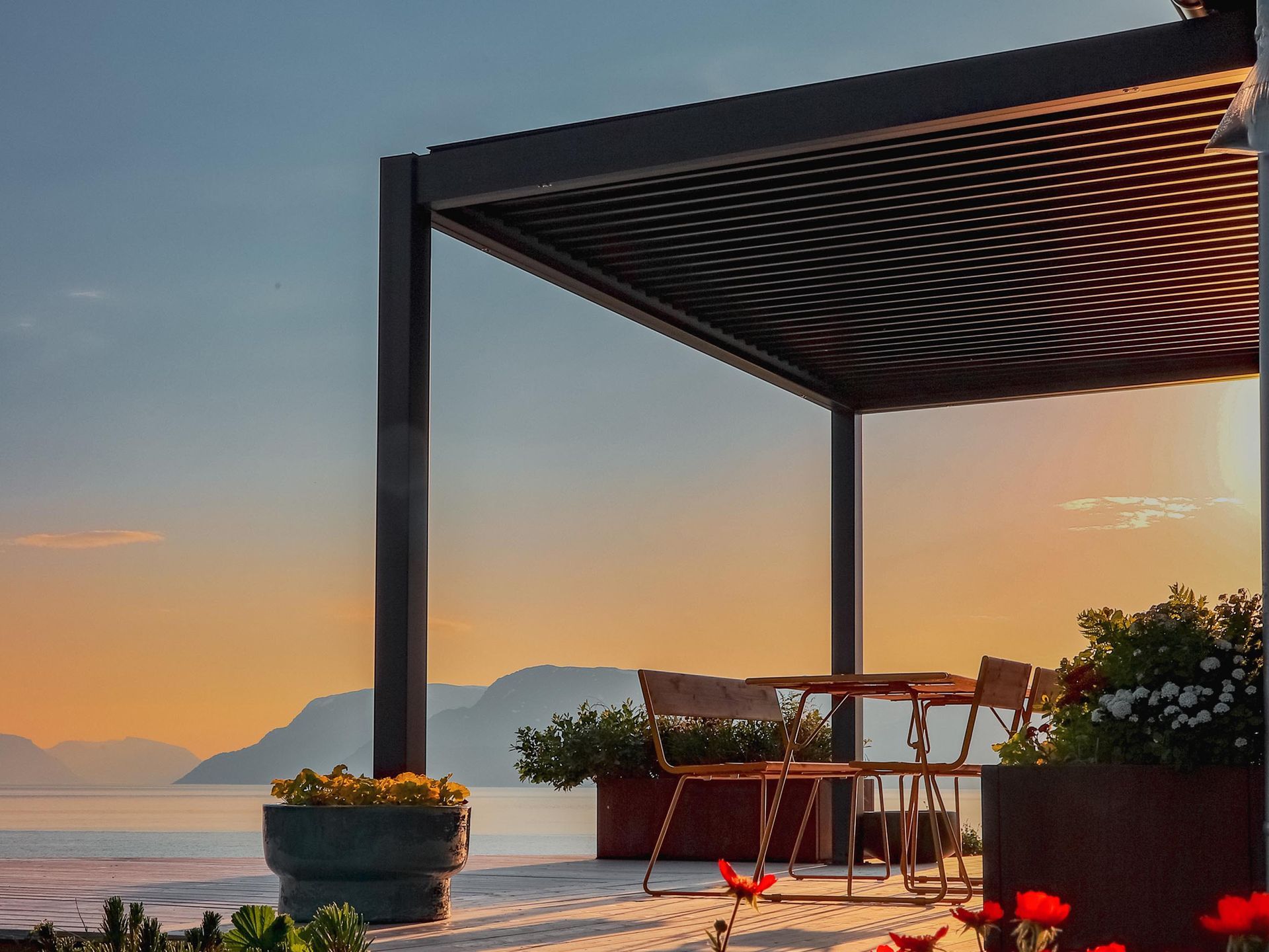 Sunset patio with a striped pergola, potted flowers, and mountain views over the water