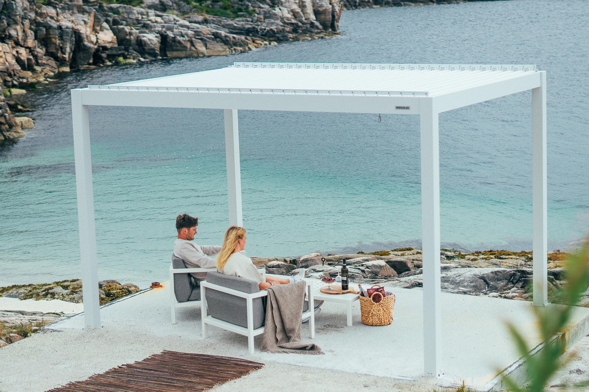 Couple seated under a white canopy by the rocky seaside, facing turquoise water