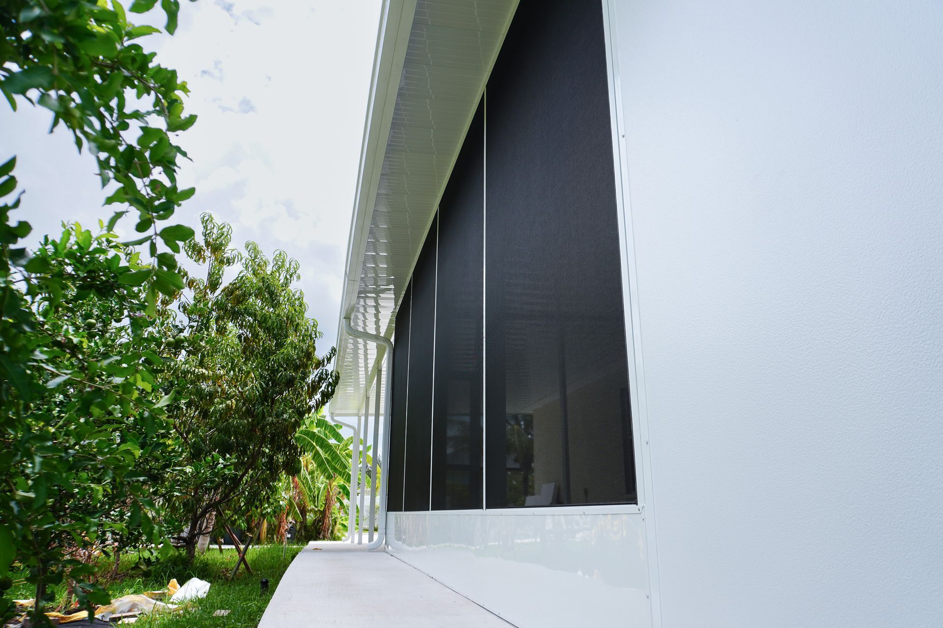 Modern building exterior with white walls, dark windows, and green trees along a walkway