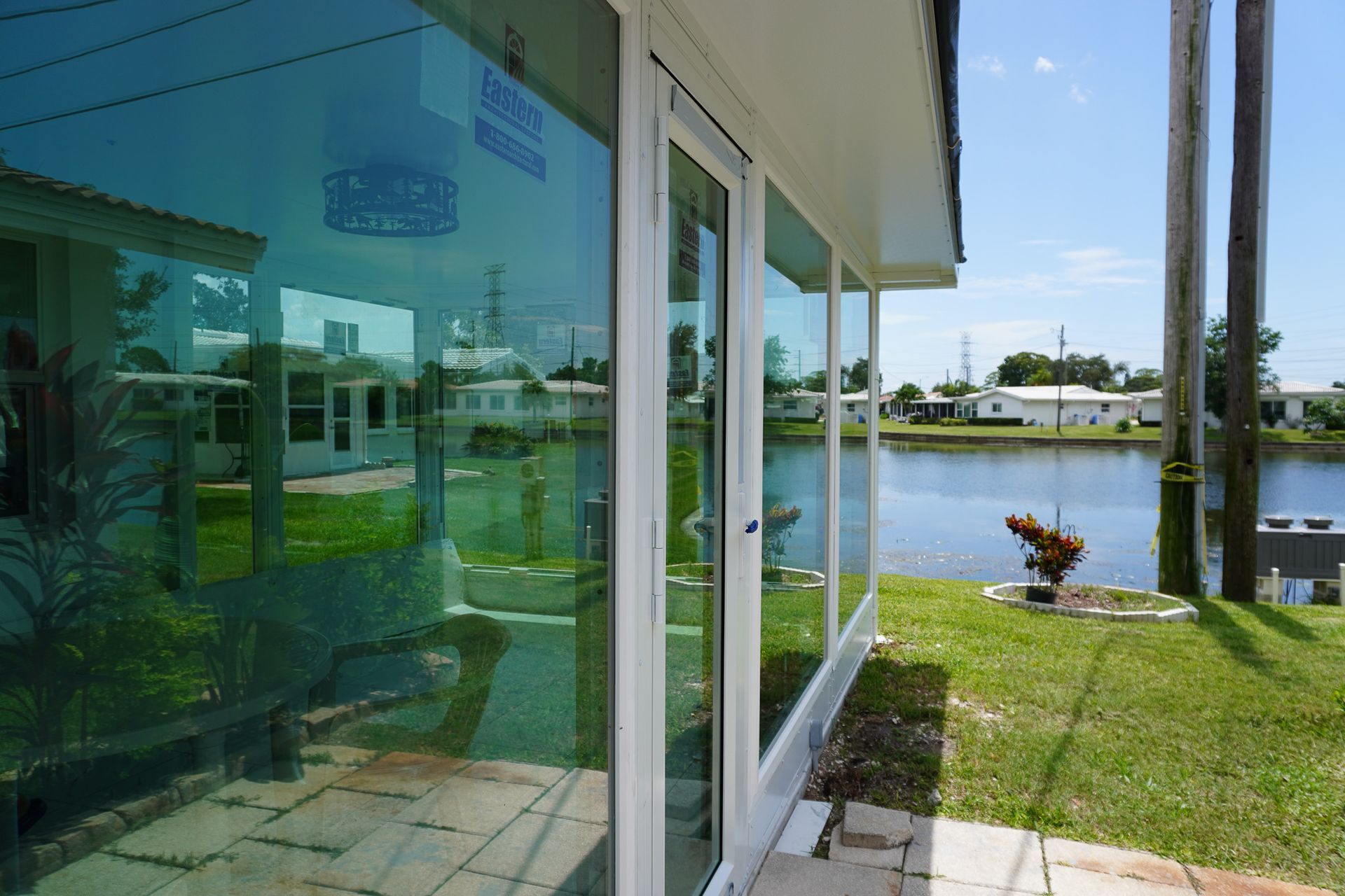 Glass-walled building beside a canal, with a grassy patio and palm trees on a sunny day
