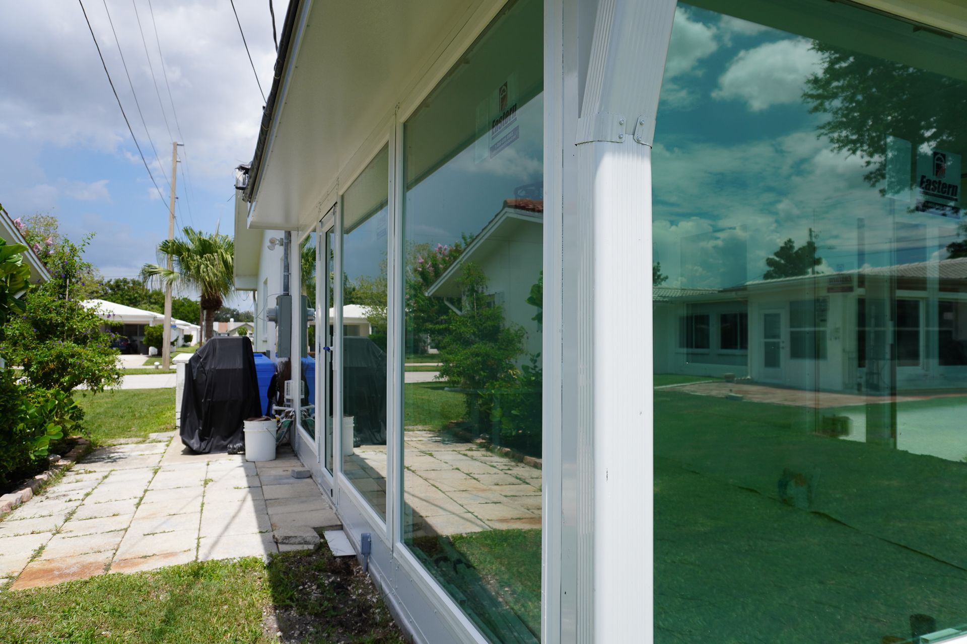 Modern house exterior with large glass windows, patio path, and outdoor grill beside greenery