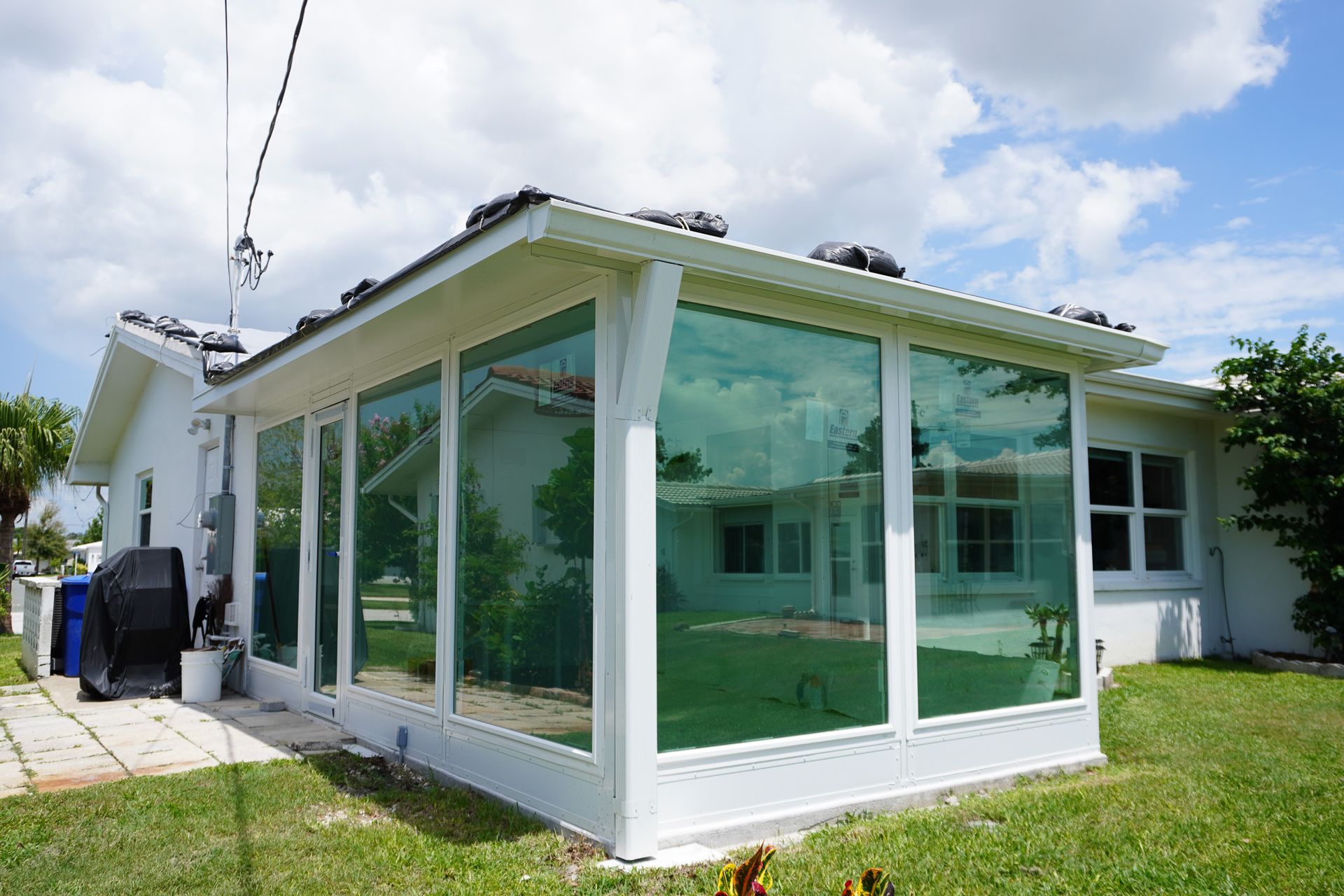 Modern white home with a glass-enclosed porch and green-tinted windows under a bright sky