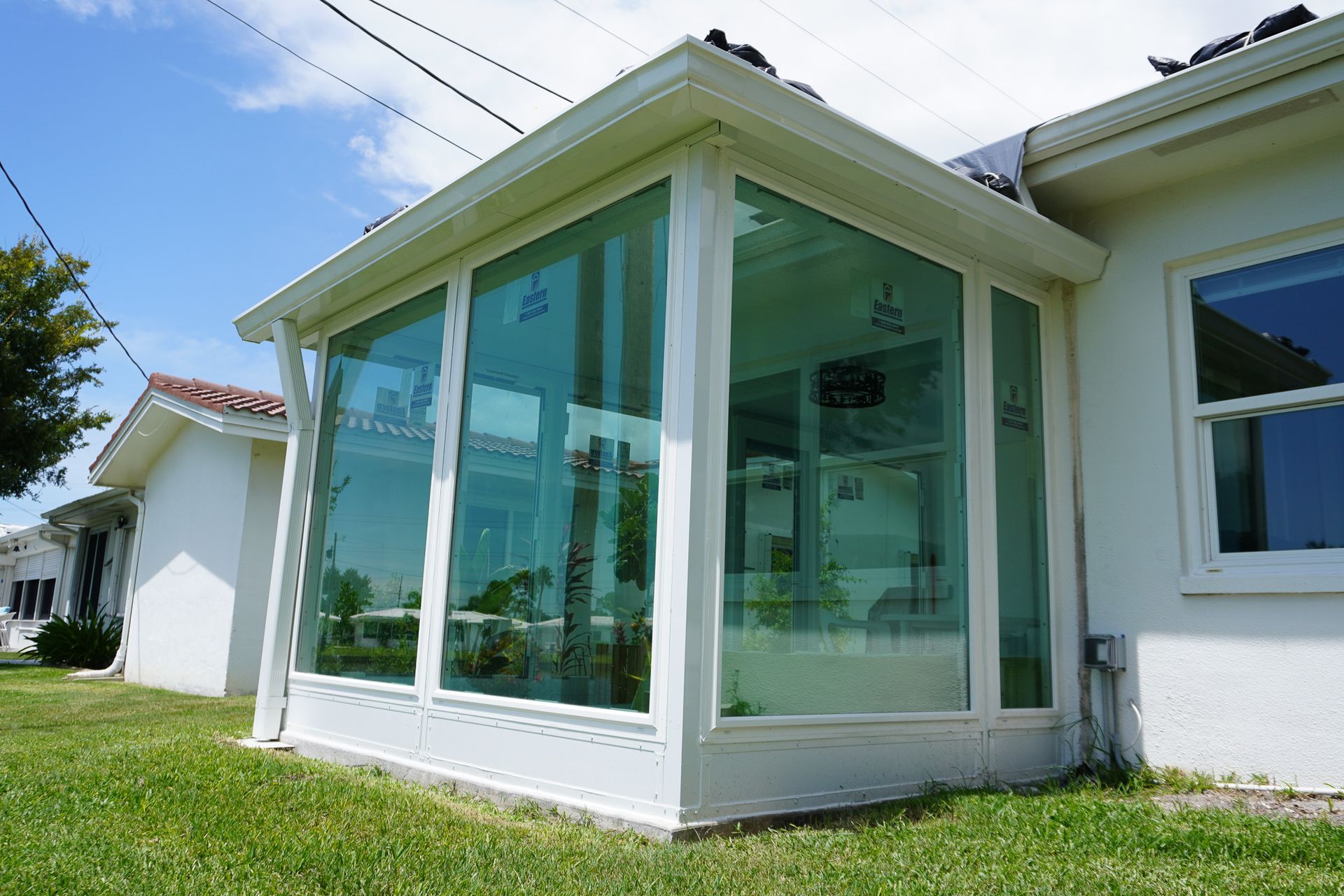 White sunroom addition with large glass windows on a grassy lawn under a blue sky