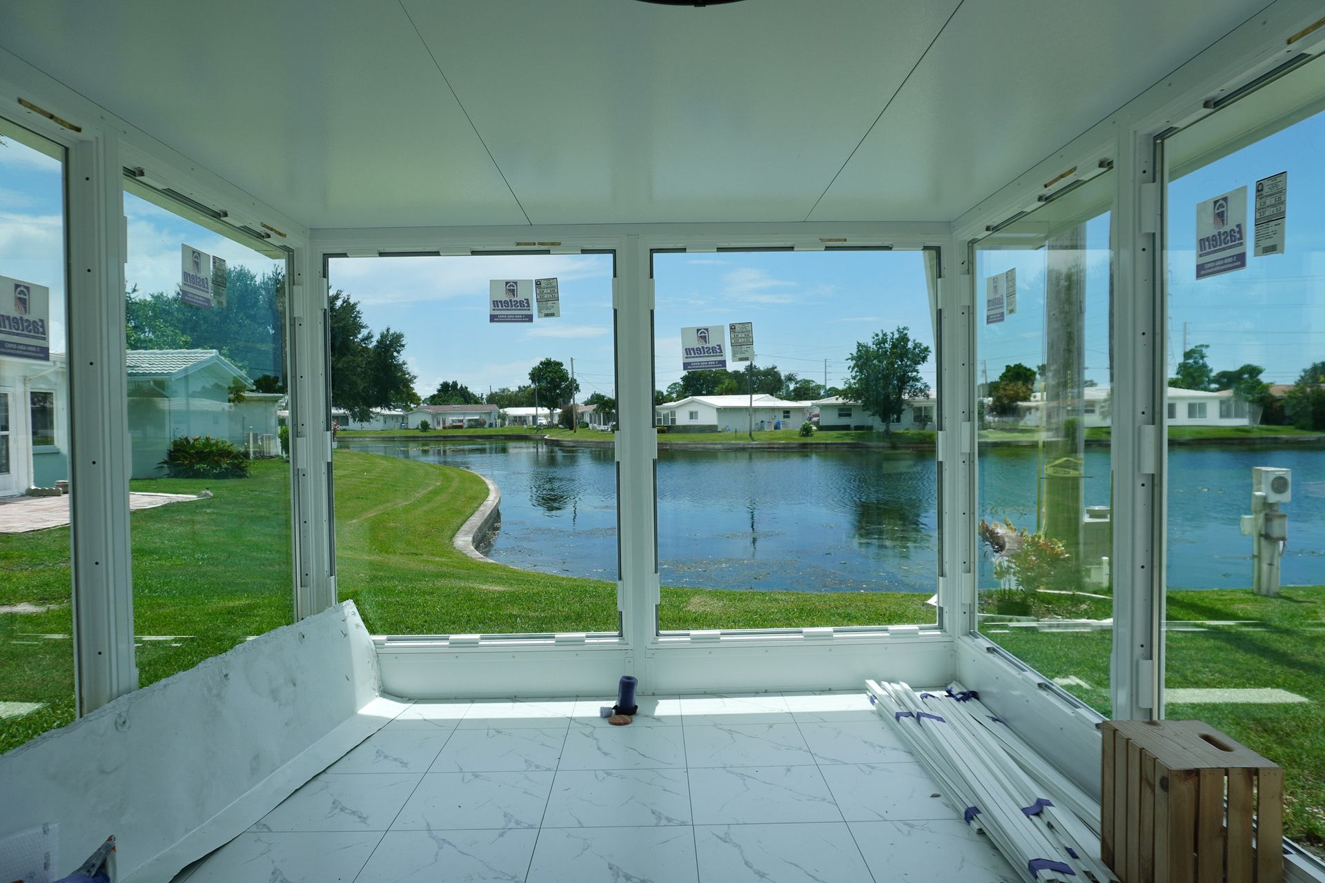White screened porch overlooking a pond and grassy shore, with open doors and city buildings in the distance