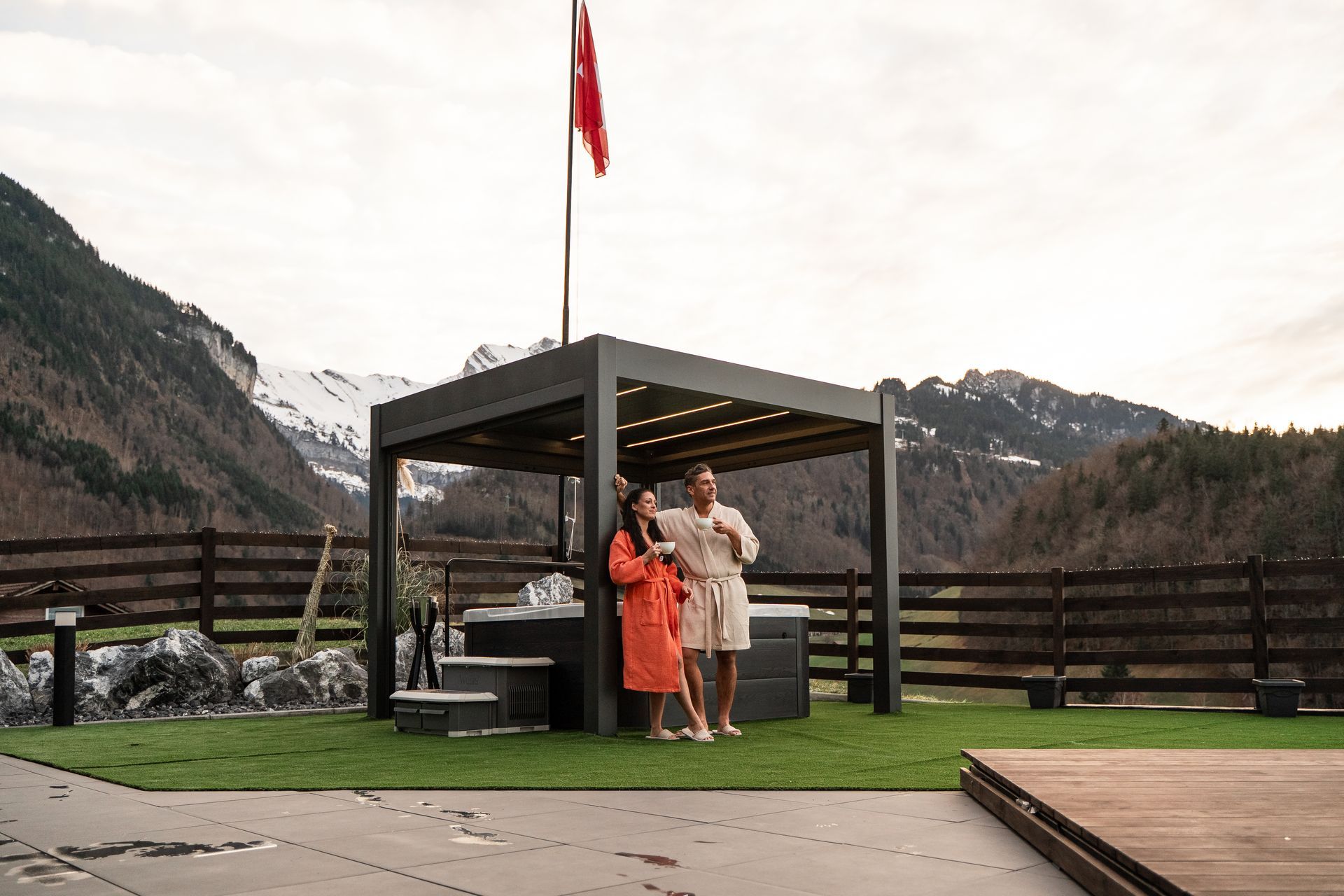 Two people posing under a flagpole in a mountain overlook pavilion
