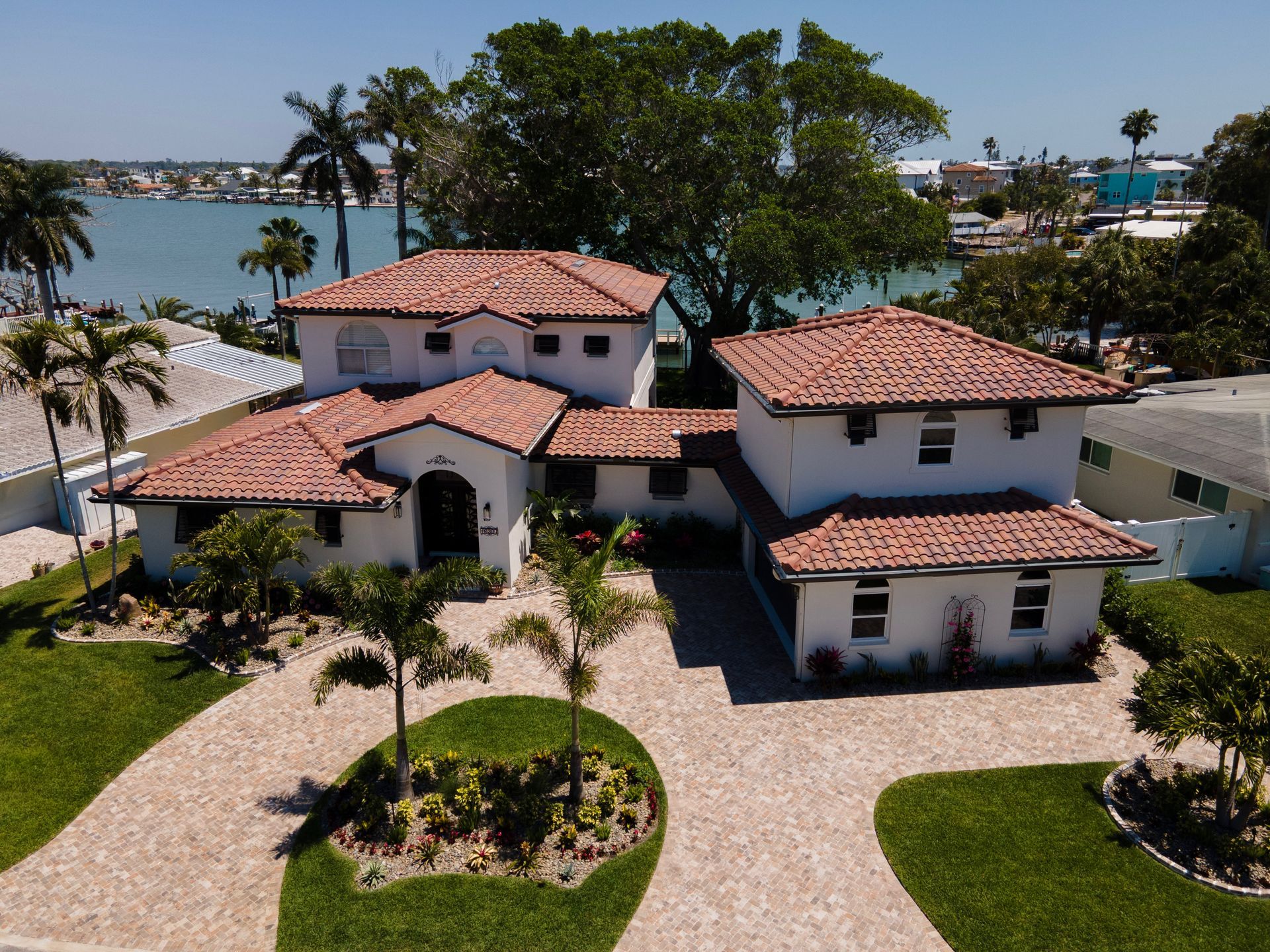 Large white stucco house with red tile roof and landscaped yard near the waterfront
