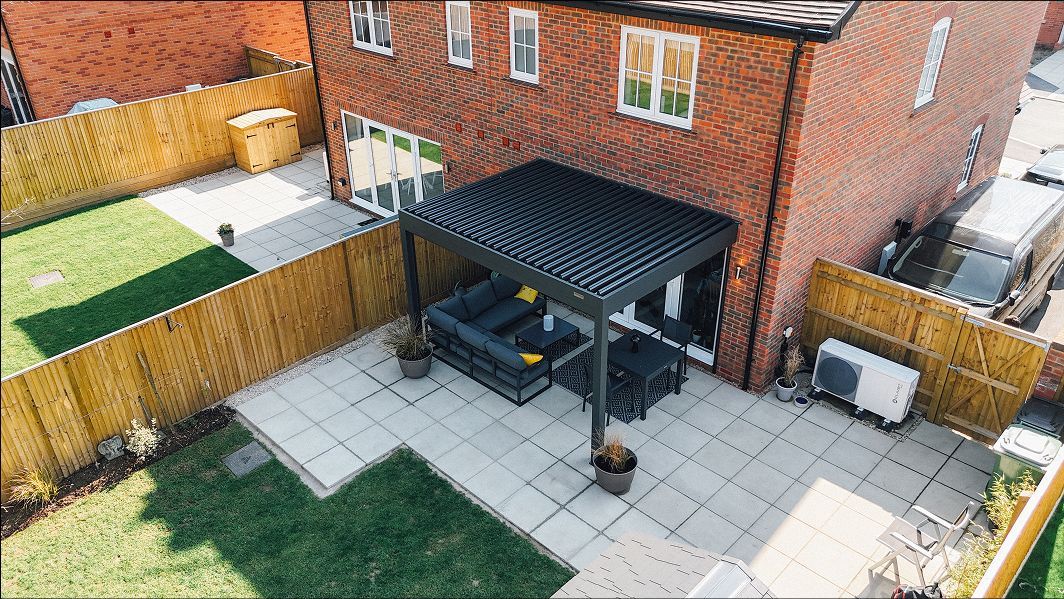 Backyard patio with paved seating area, black pergola, wooden fencing, and a brick house wall