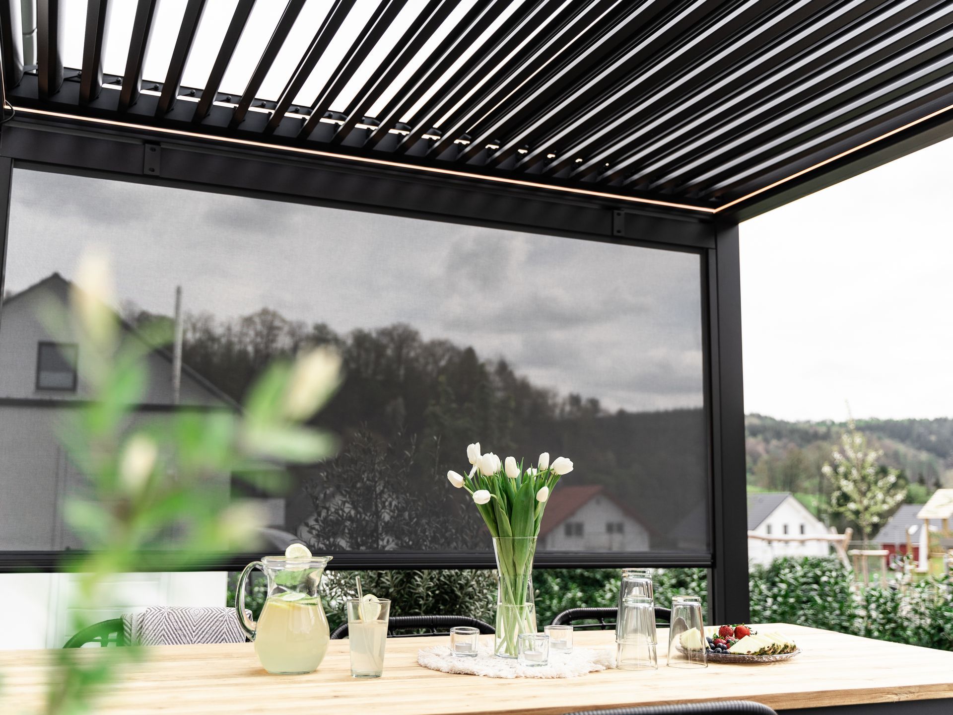 Outdoor patio table set with white flowers, drinks, and a view of hills under a pergola