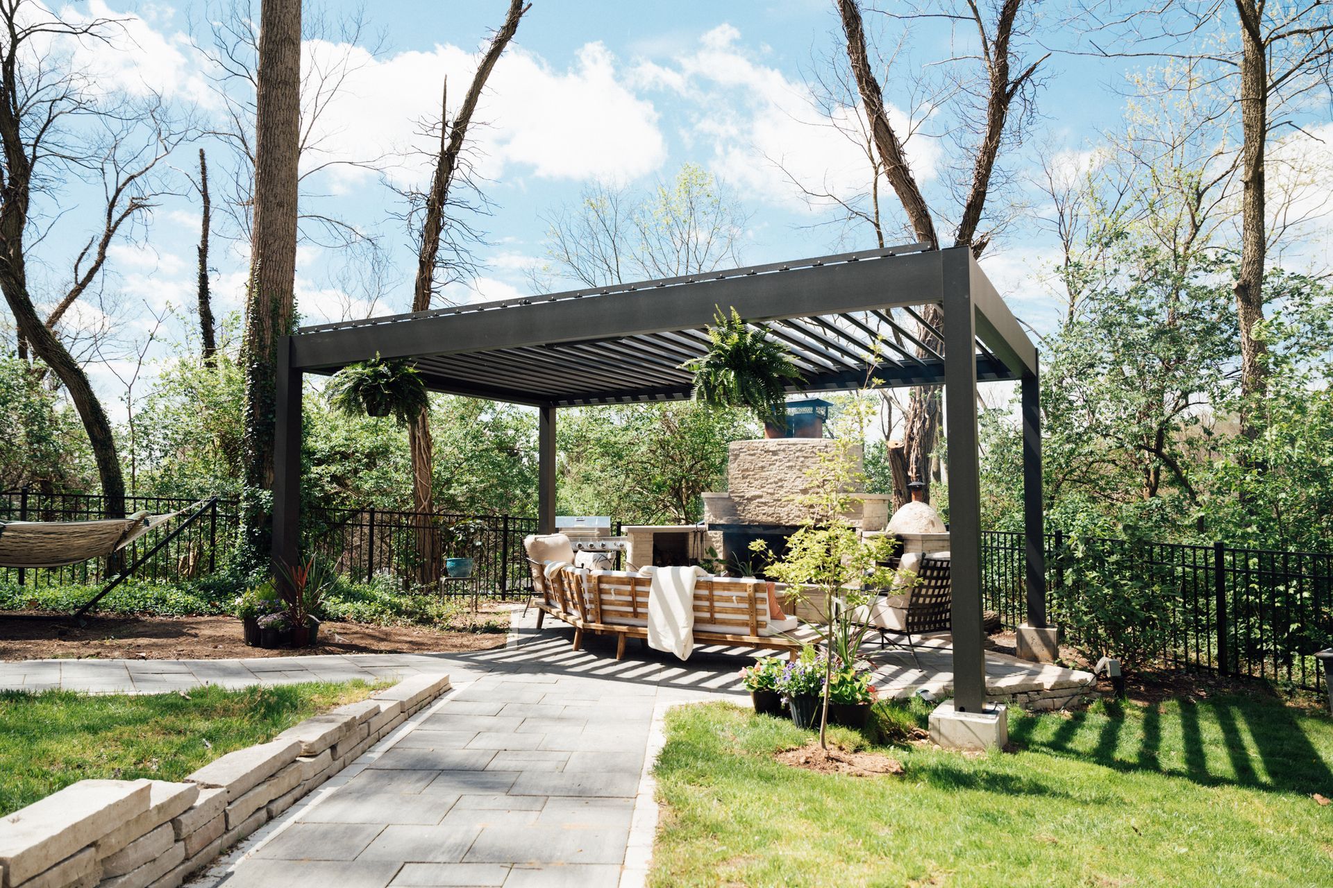 Backyard patio with pergola, wooden seating, and landscaped garden beside a paved path.