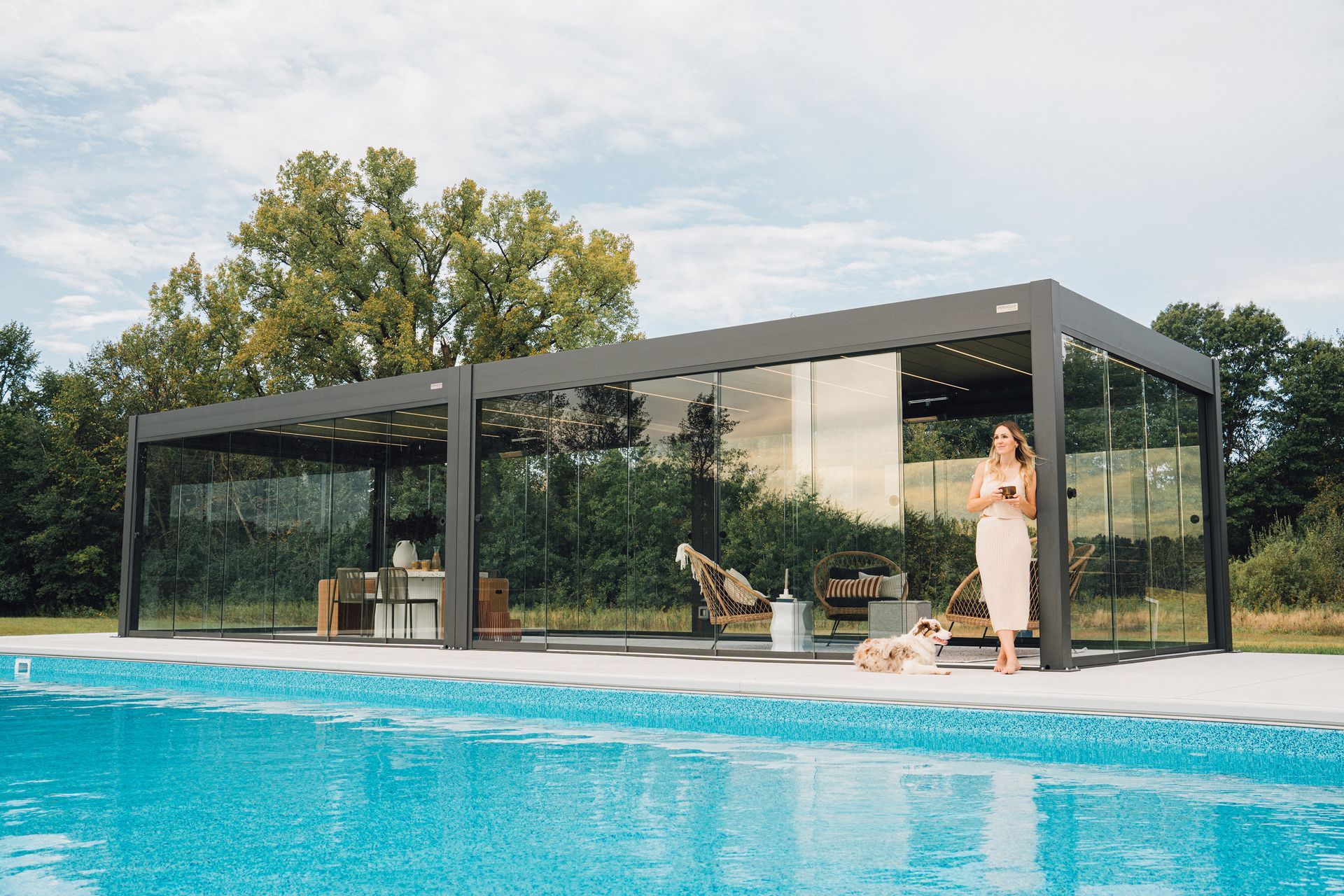 Modern glass poolside pavilion with lounge chairs beside a bright blue swimming pool