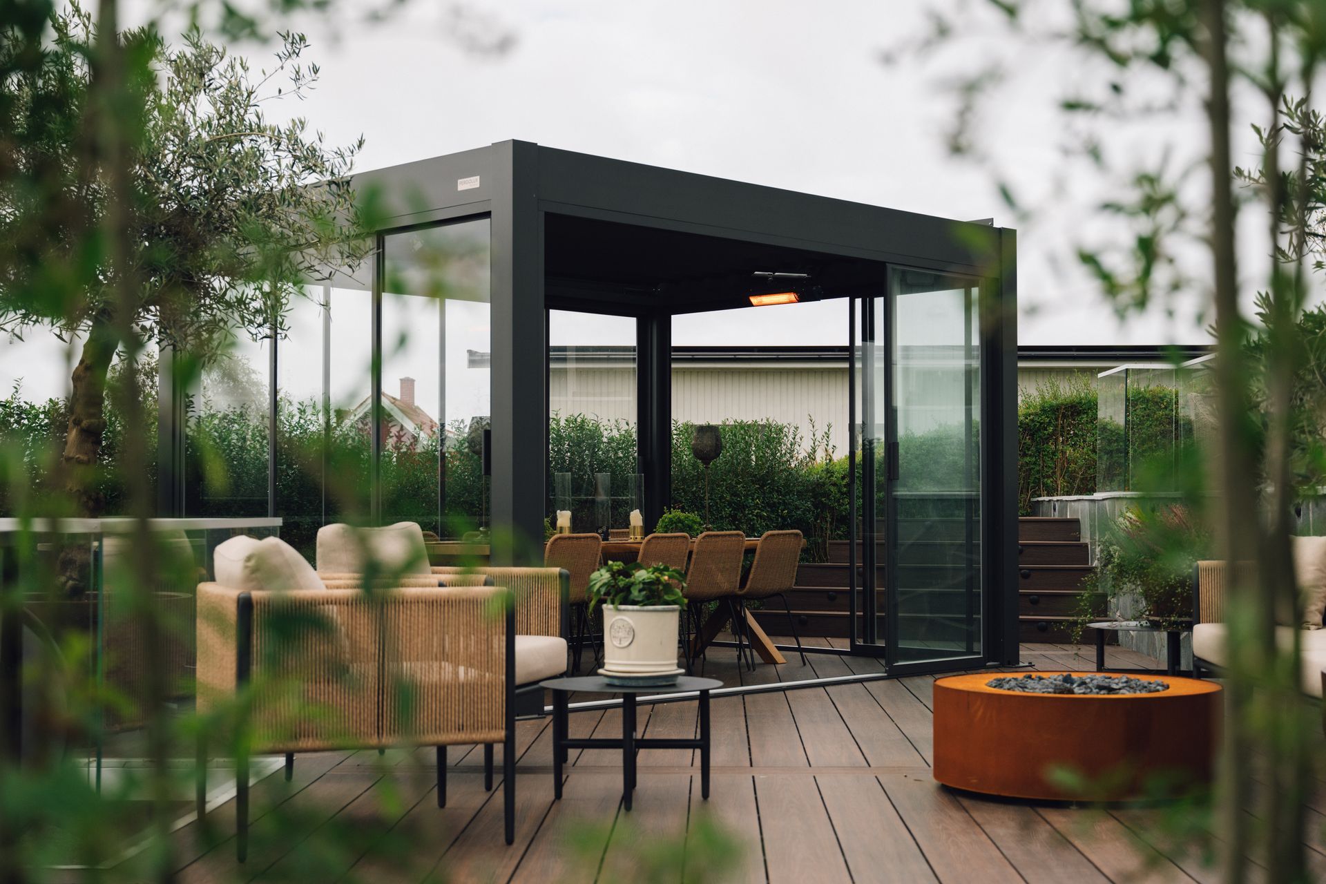 Modern outdoor patio with black pergola, wooden deck, chairs, and greenery