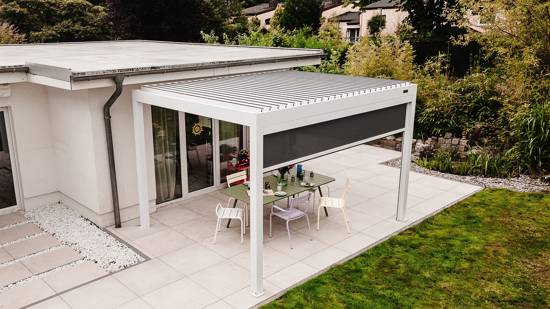 Modern white patio pergola with outdoor dining table beside a house and green lawn