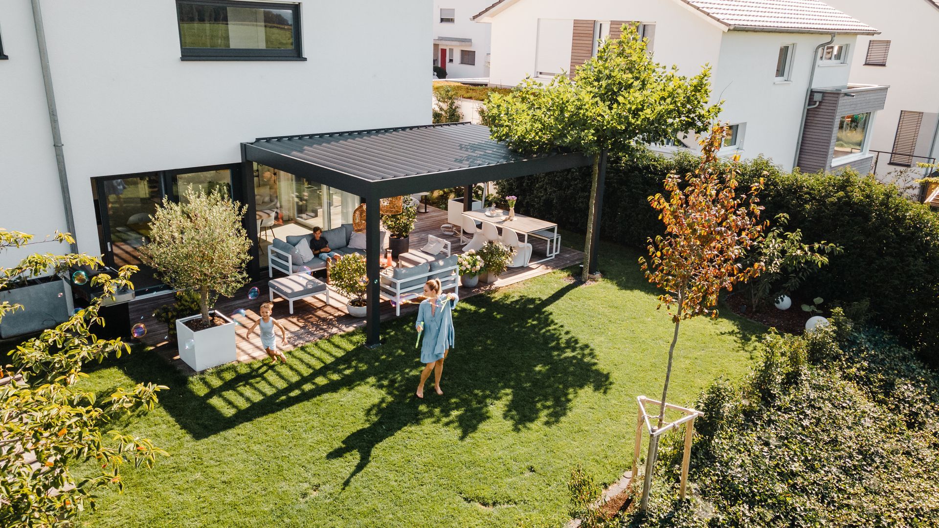 Backyard patio with pergola, outdoor dining table, and a person standing on the lawn