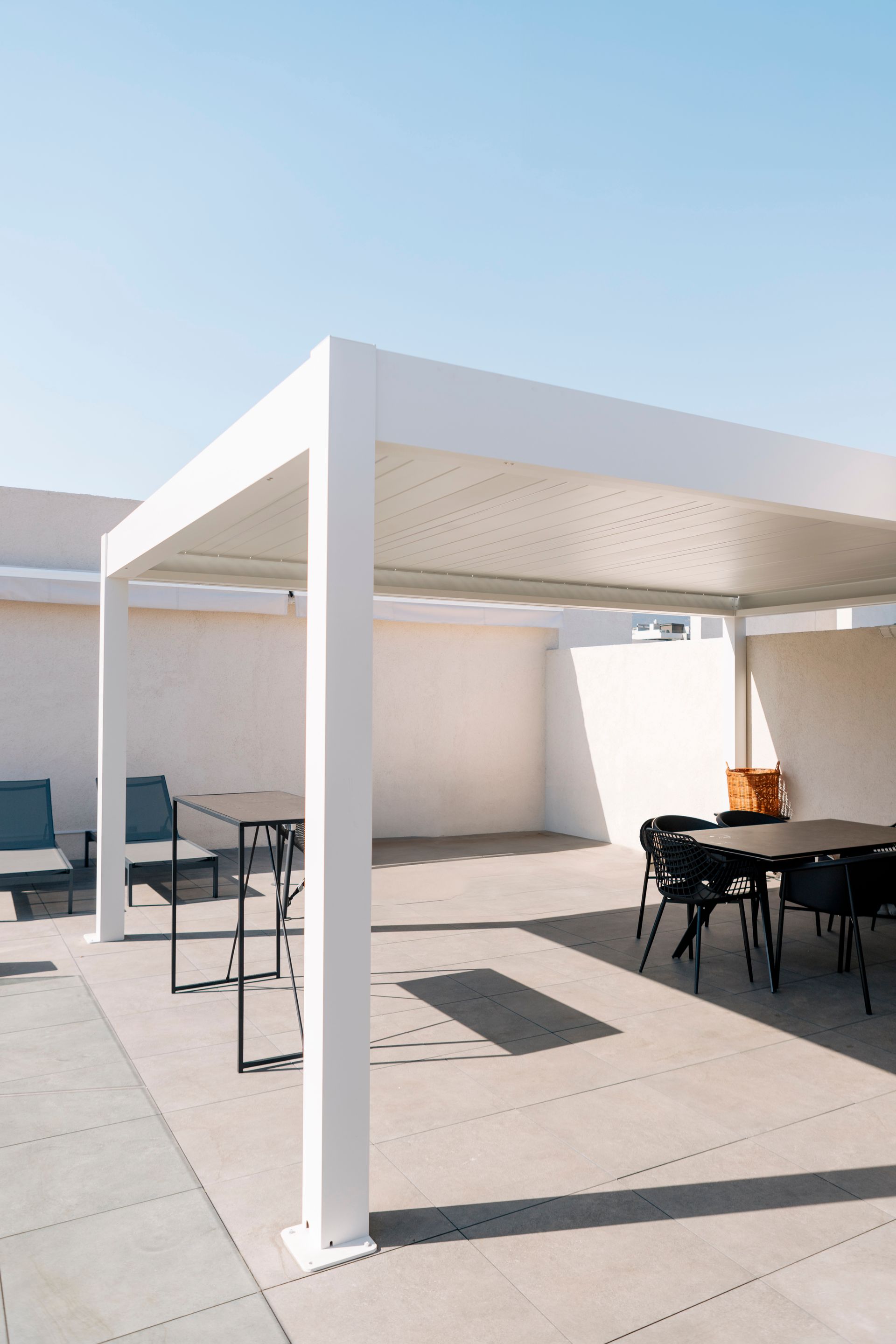 White pergola-covered patio with black tables and chairs in bright sunlight