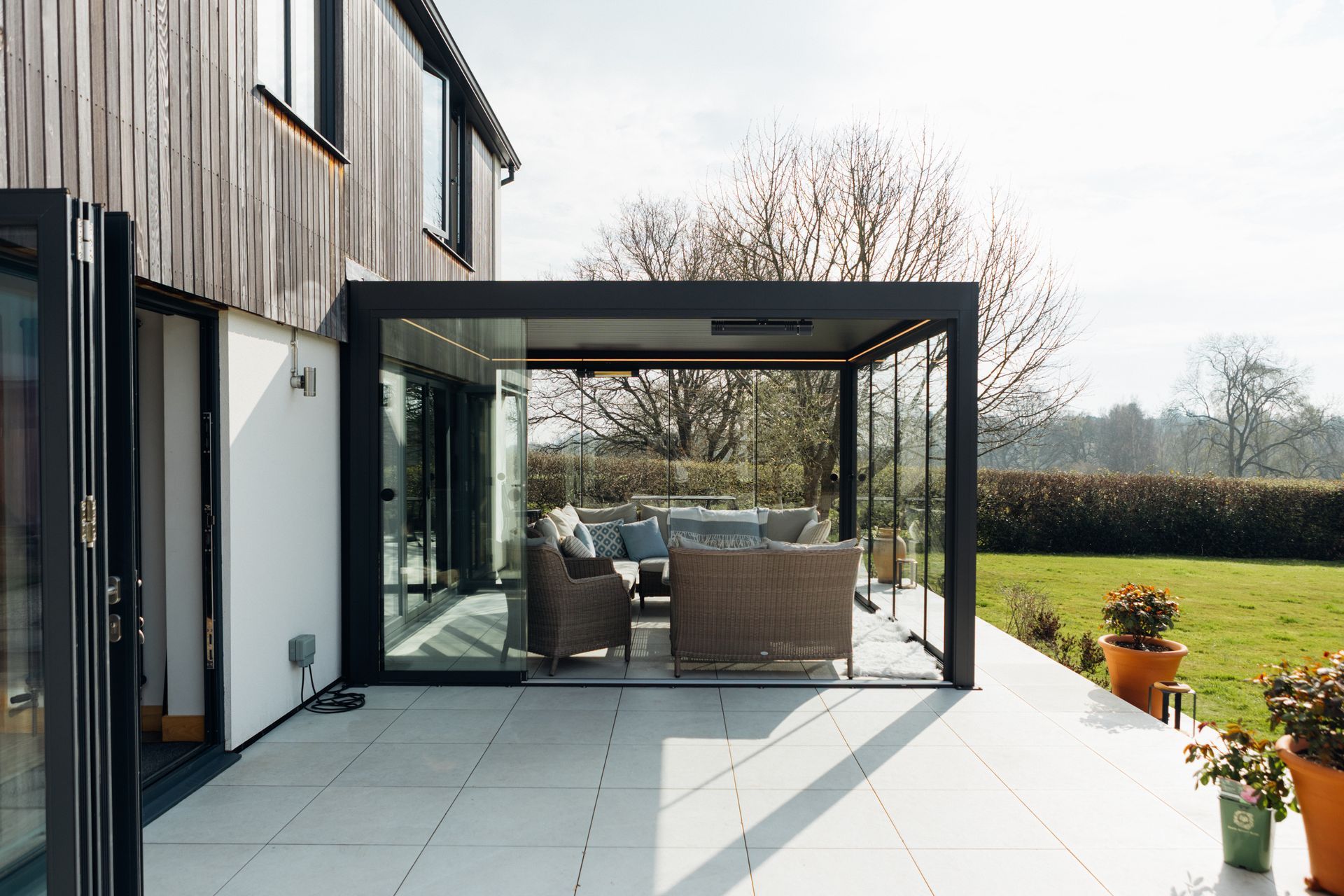 Modern house patio with glass pergola, outdoor seating, and a view of the garden