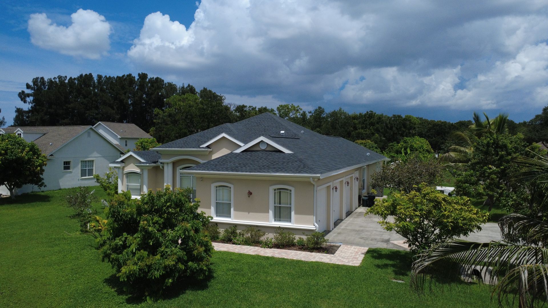 Single-story beige house with gray roof and green lawn under a cloudy sky