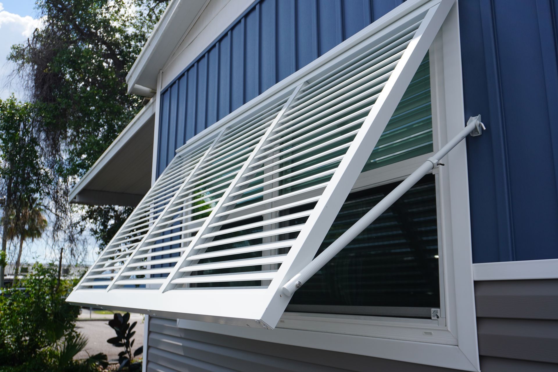 White louvered window awning on a blue house exterior