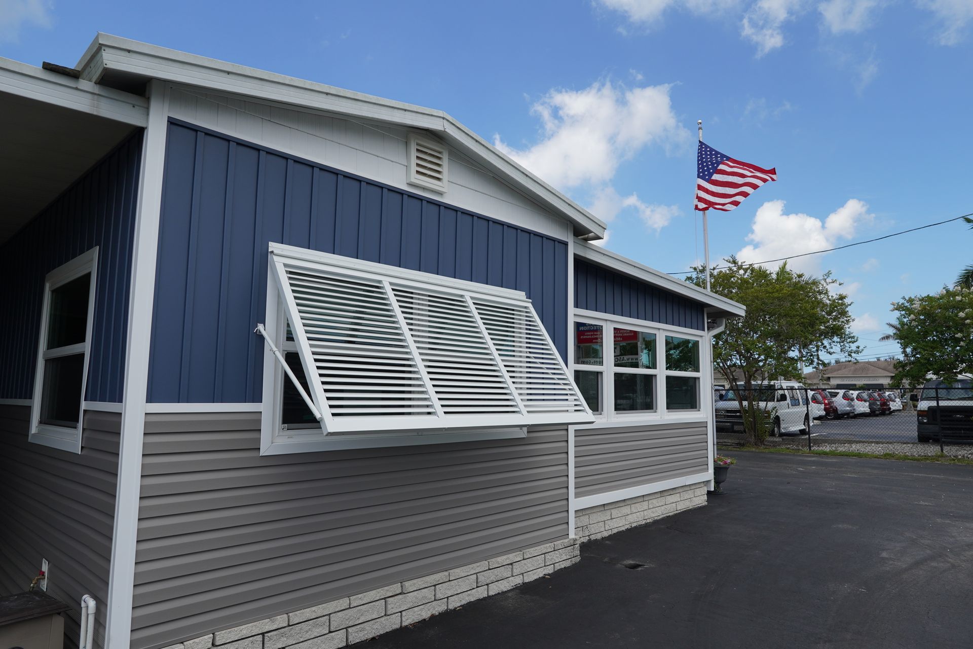 Blue-and-gray building with open awning windows and an American flag on a pole outside