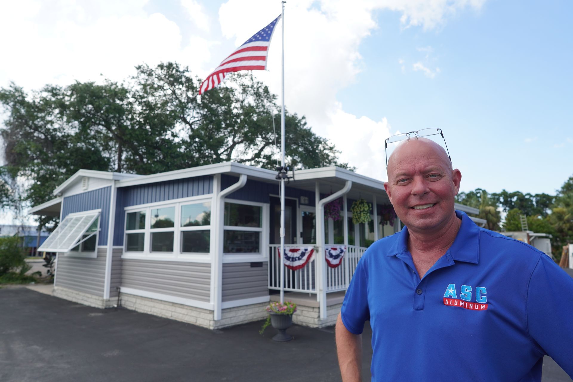 Man in blue shirt standing by a small building with patriotic bunting and an American flag waving overhead