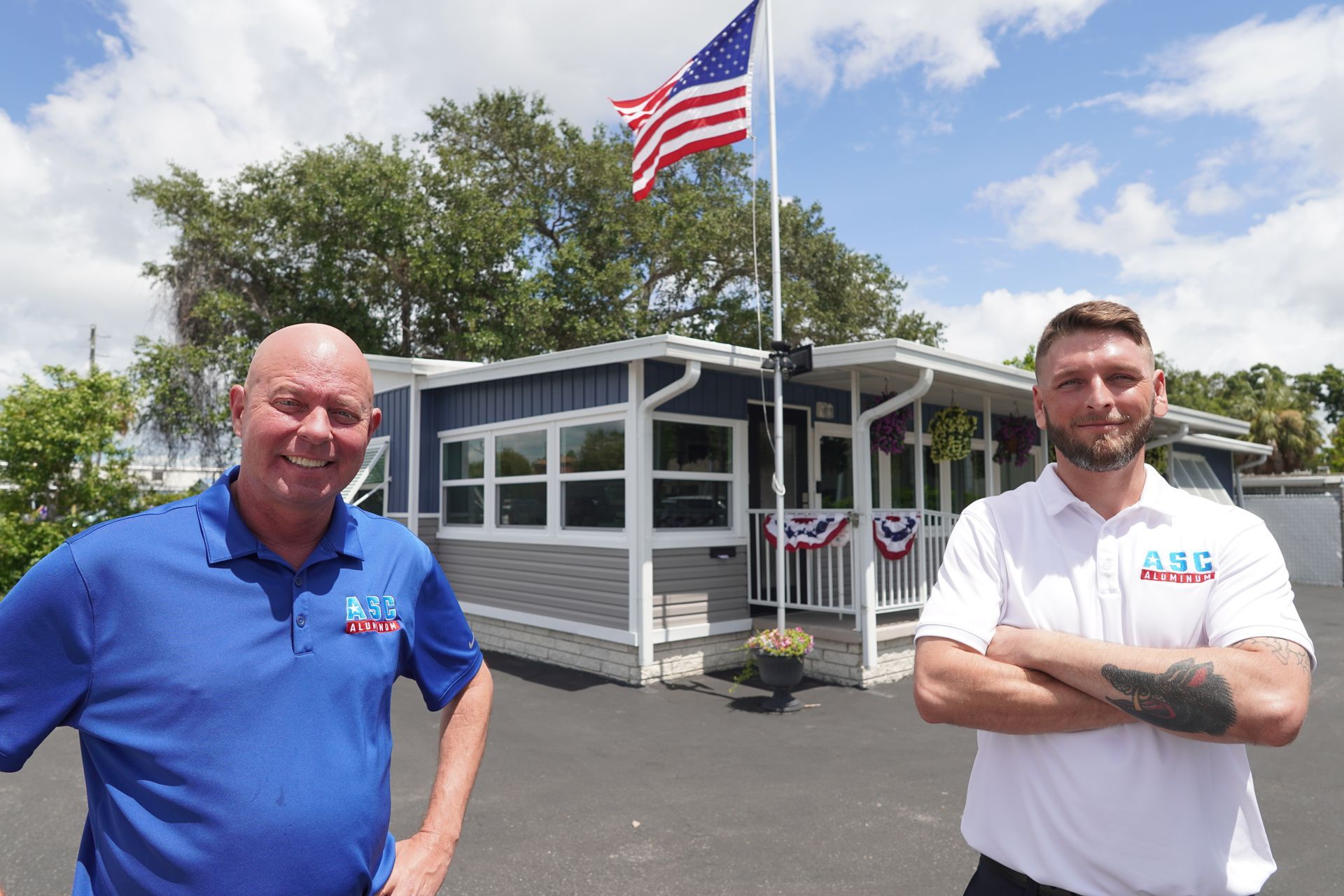 Two men standing outside a small building with an American flag flying overhead