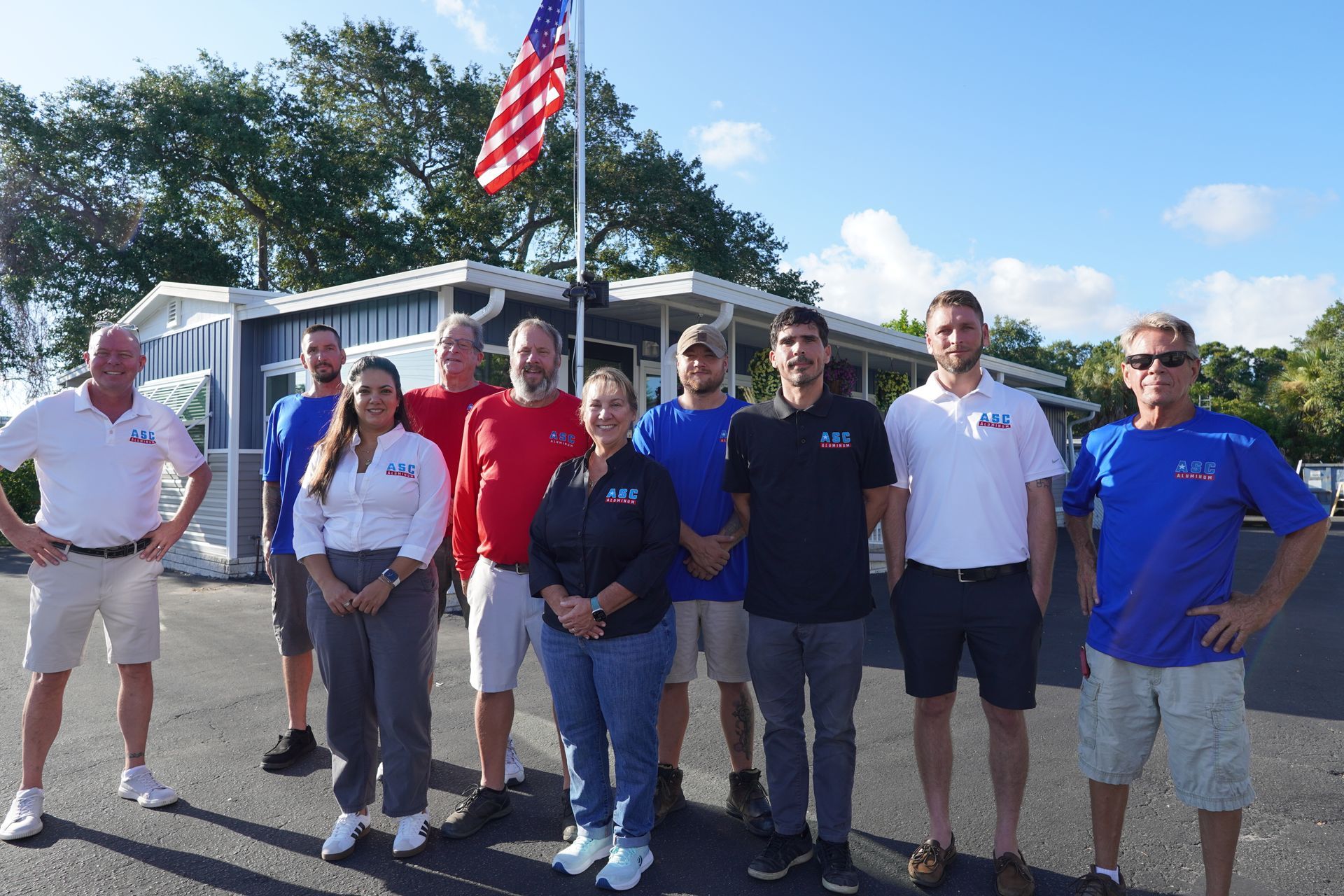 Group of people standing outdoors in front of RVs, with an American flag waving overhead.