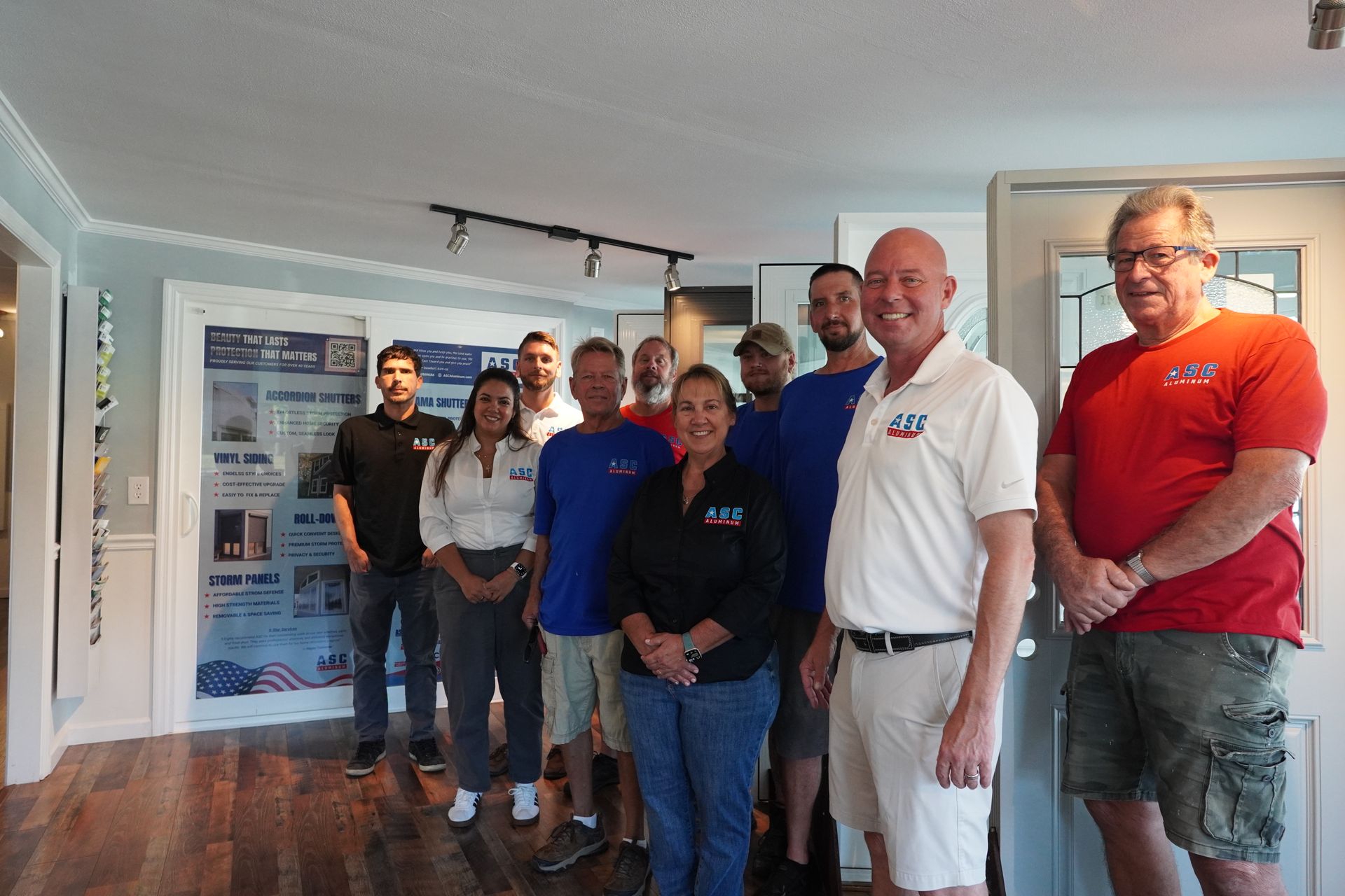 Group of people standing indoors at an event, smiling in casual clothes, with a banner in the background