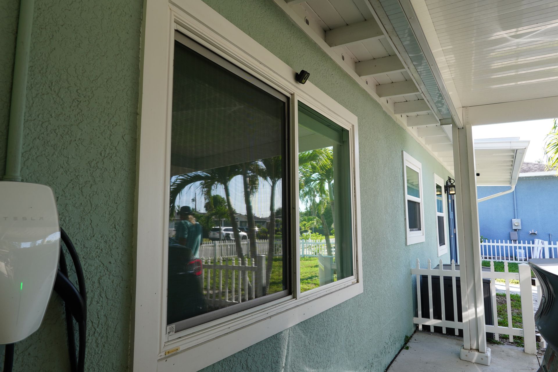 White-framed window and porch with green stucco wall, railing, and view of palm trees outside