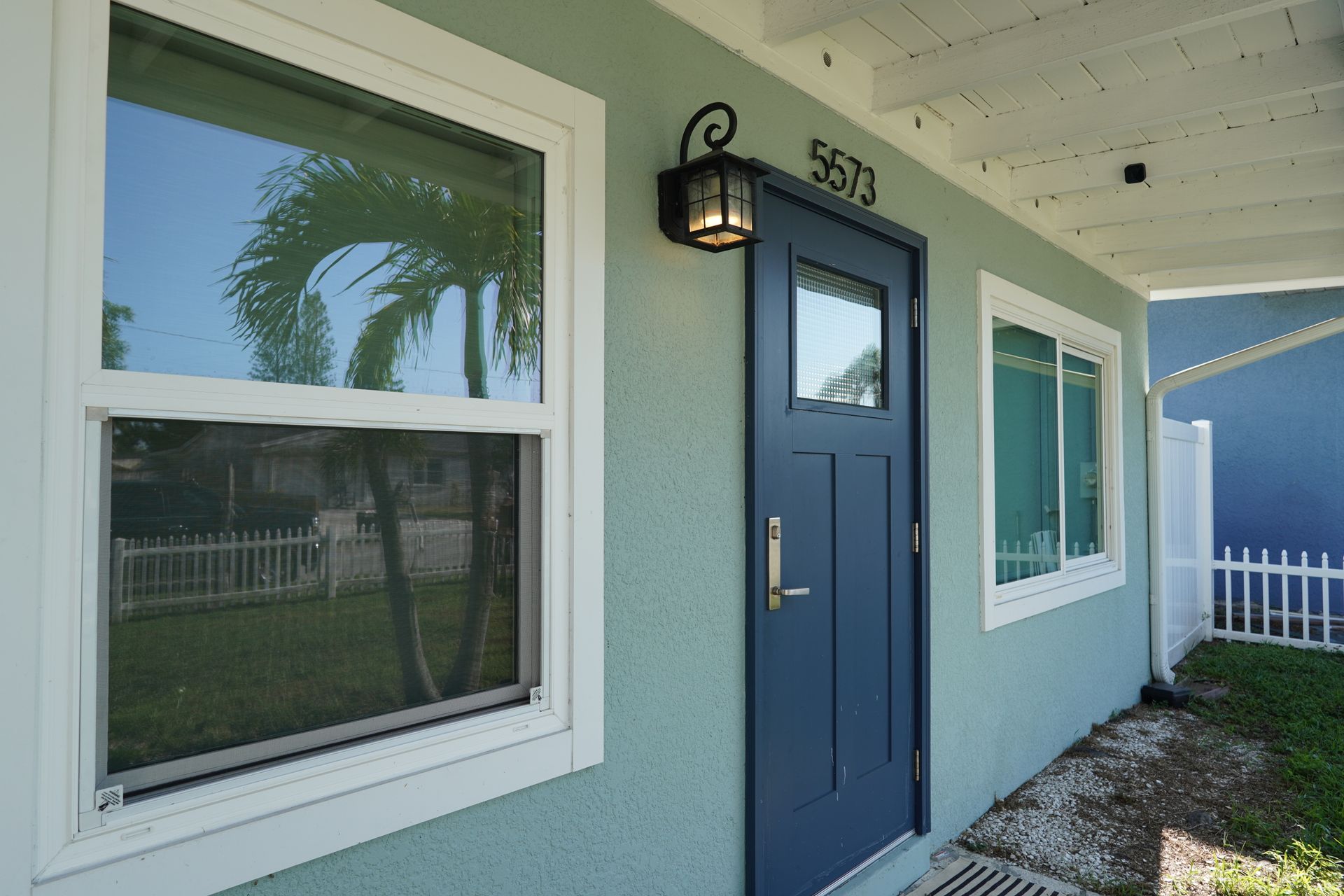 Blue front door and windows on a light blue house exterior with a porch light and house number 5833.