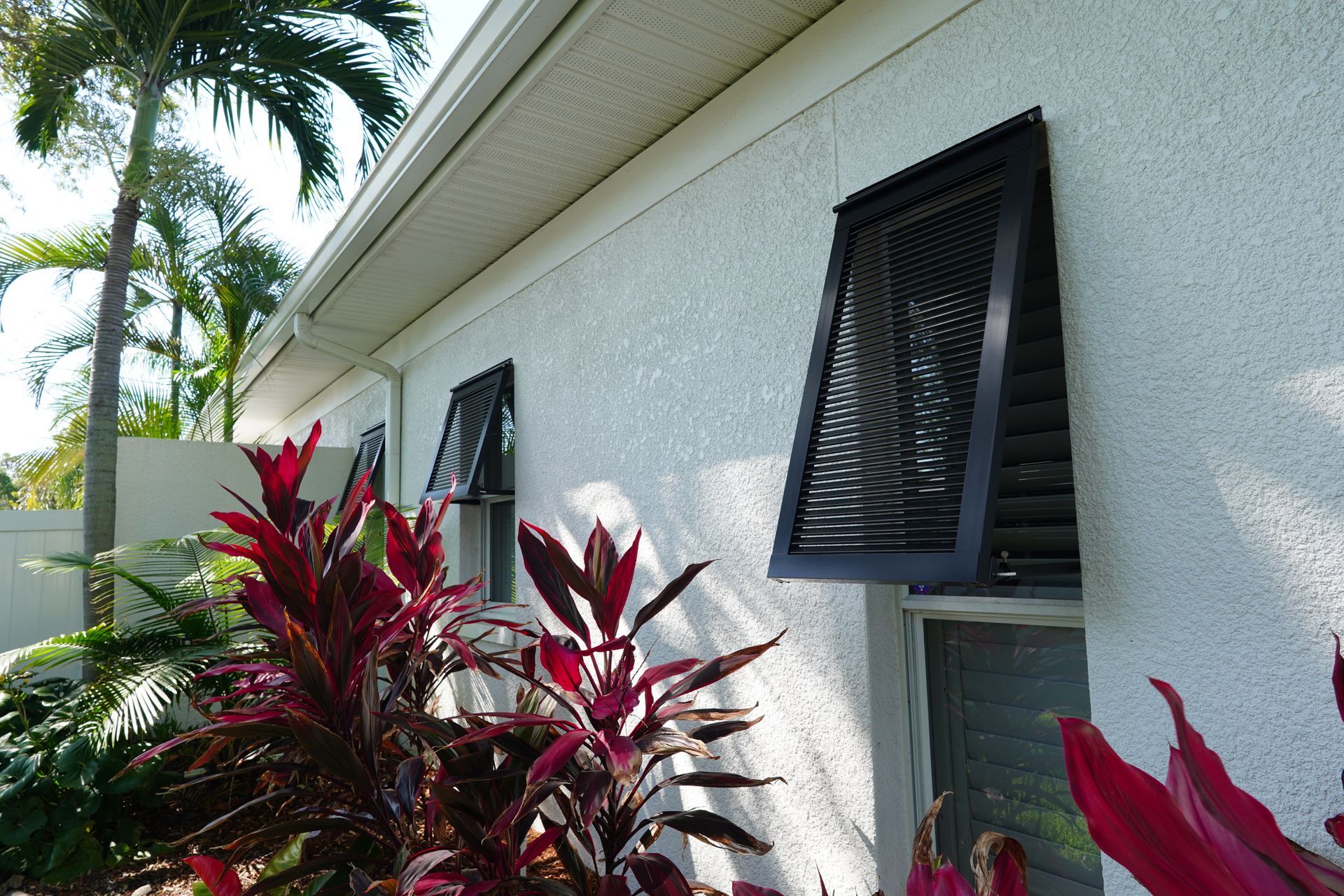 White house exterior with open louvered windows and red tropical plants in front