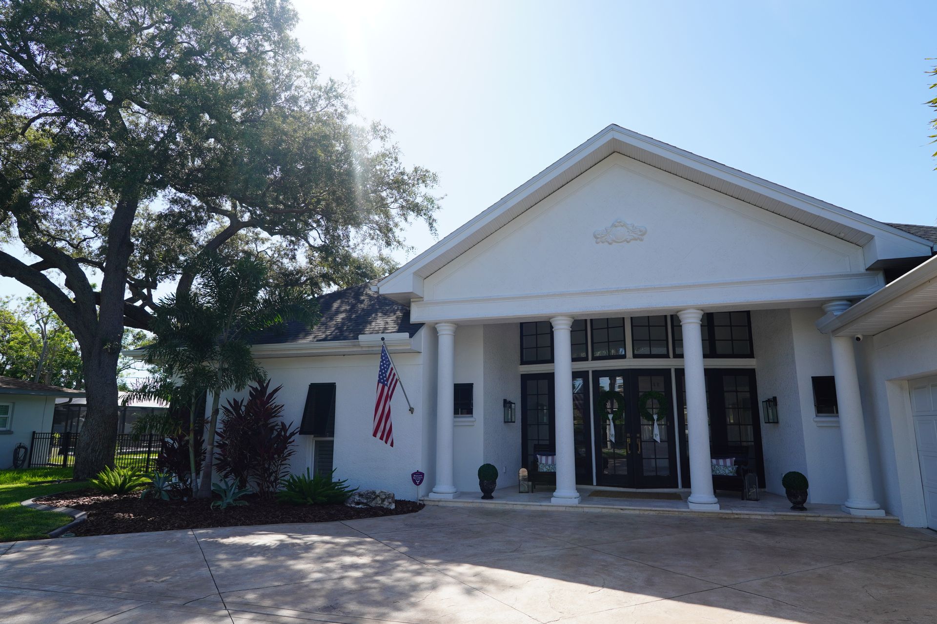White building entrance with columns, glass doors, and an American flag in front under a sunny sky
