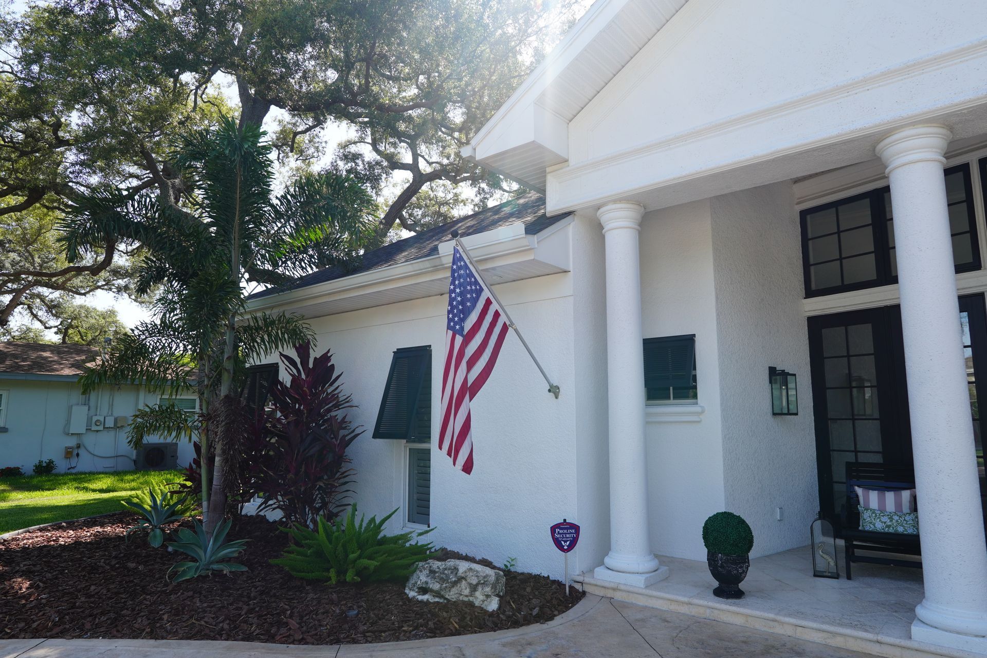 White house entrance with columns, American flag, and landscaped front yard in bright sunlight