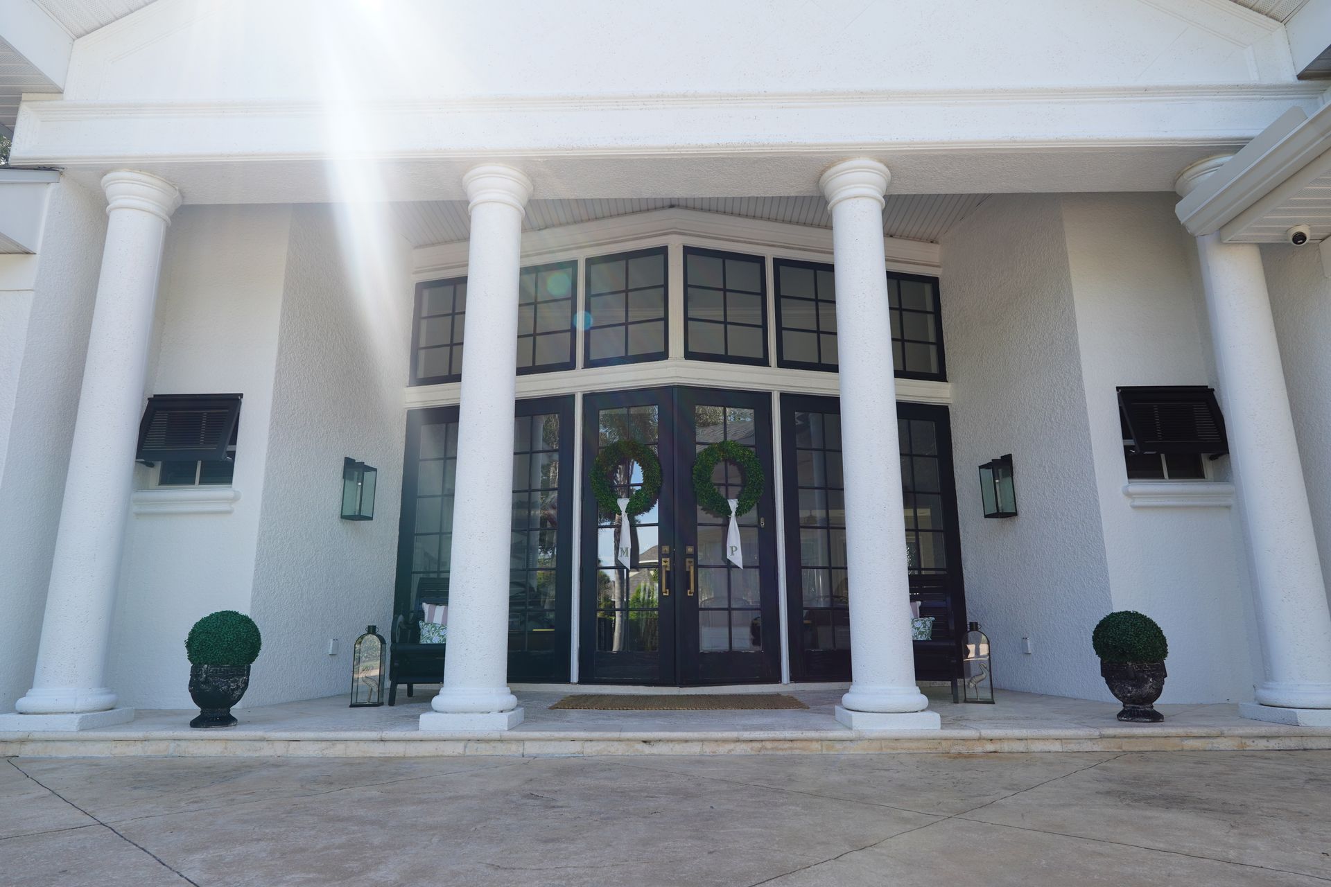 White-columned building entrance with glass double doors and potted shrubs