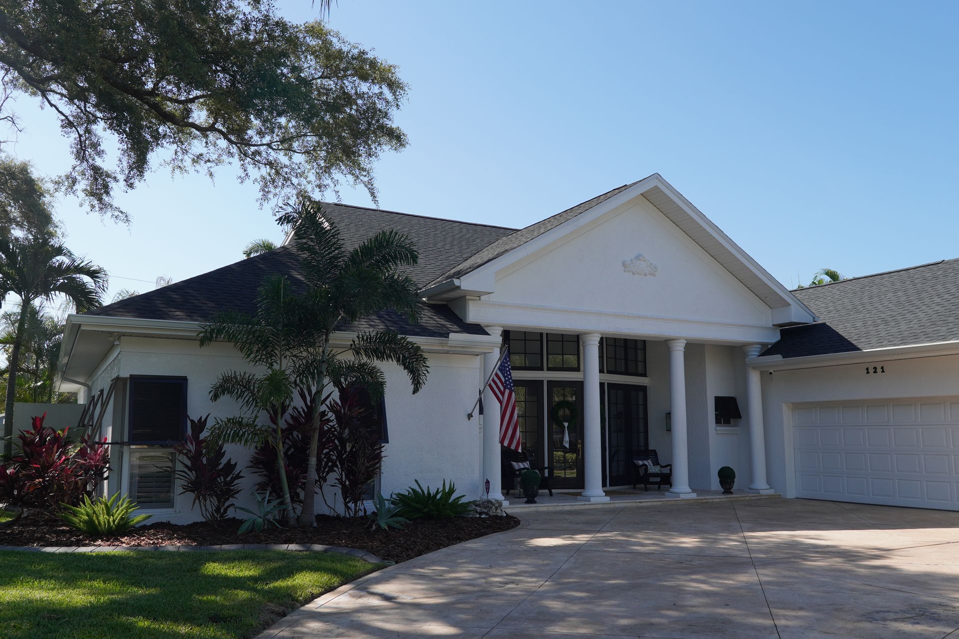 White suburban house with a gabled entry, garage, driveway, and palm trees in front
