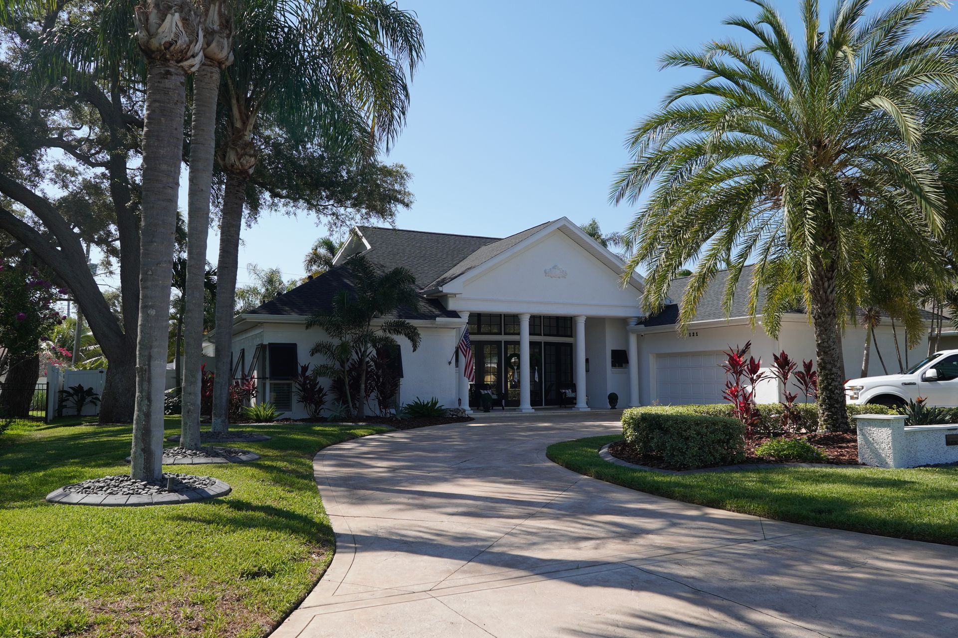 Single-story white house with a curved driveway and palm trees in the front yard