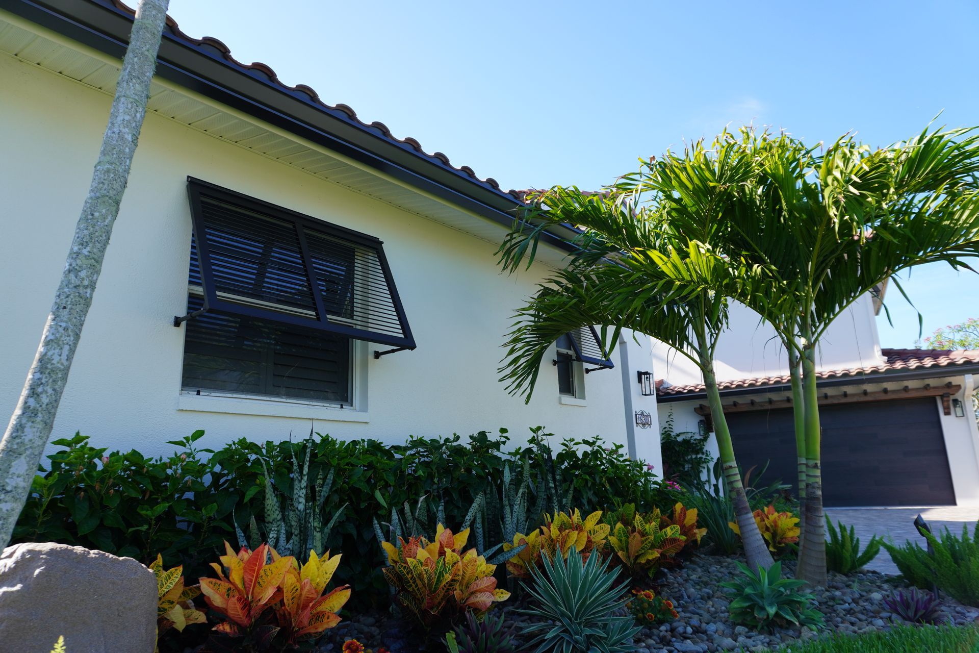 Tropical house exterior with white walls, black window awning, and lush green and orange landscaping