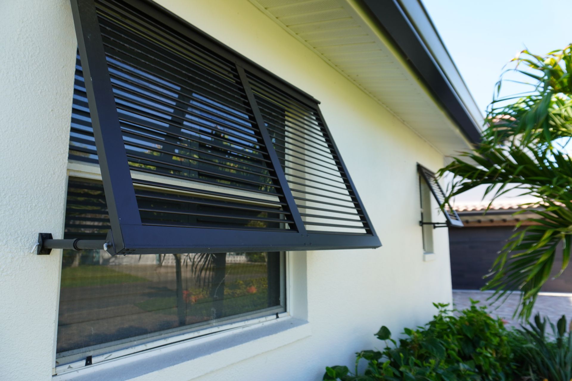 House exterior with black louvered windows and white walls along a garden walkway