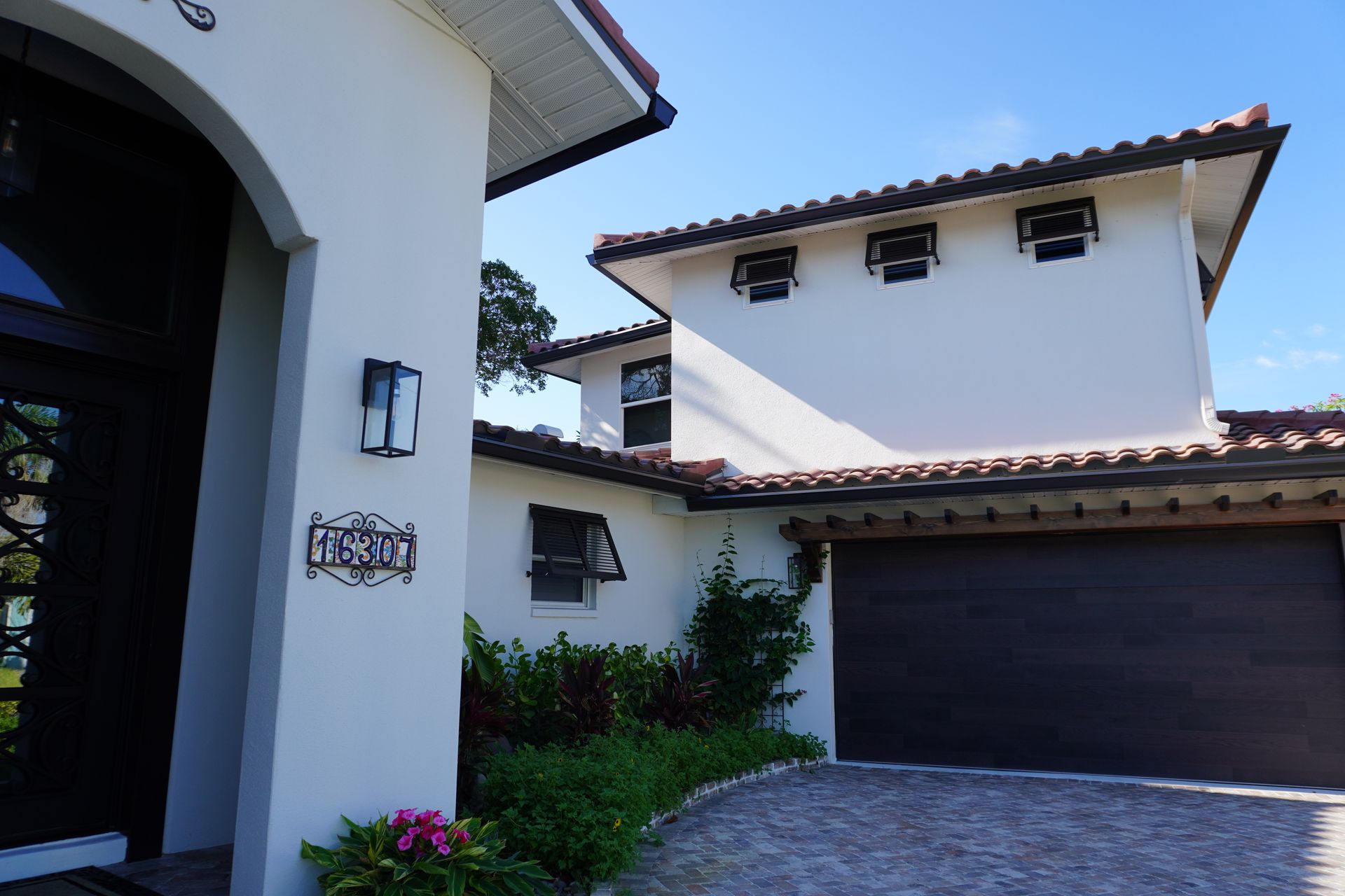 Spanish-style house exterior with white stucco walls, red tile roof, and dark garage door