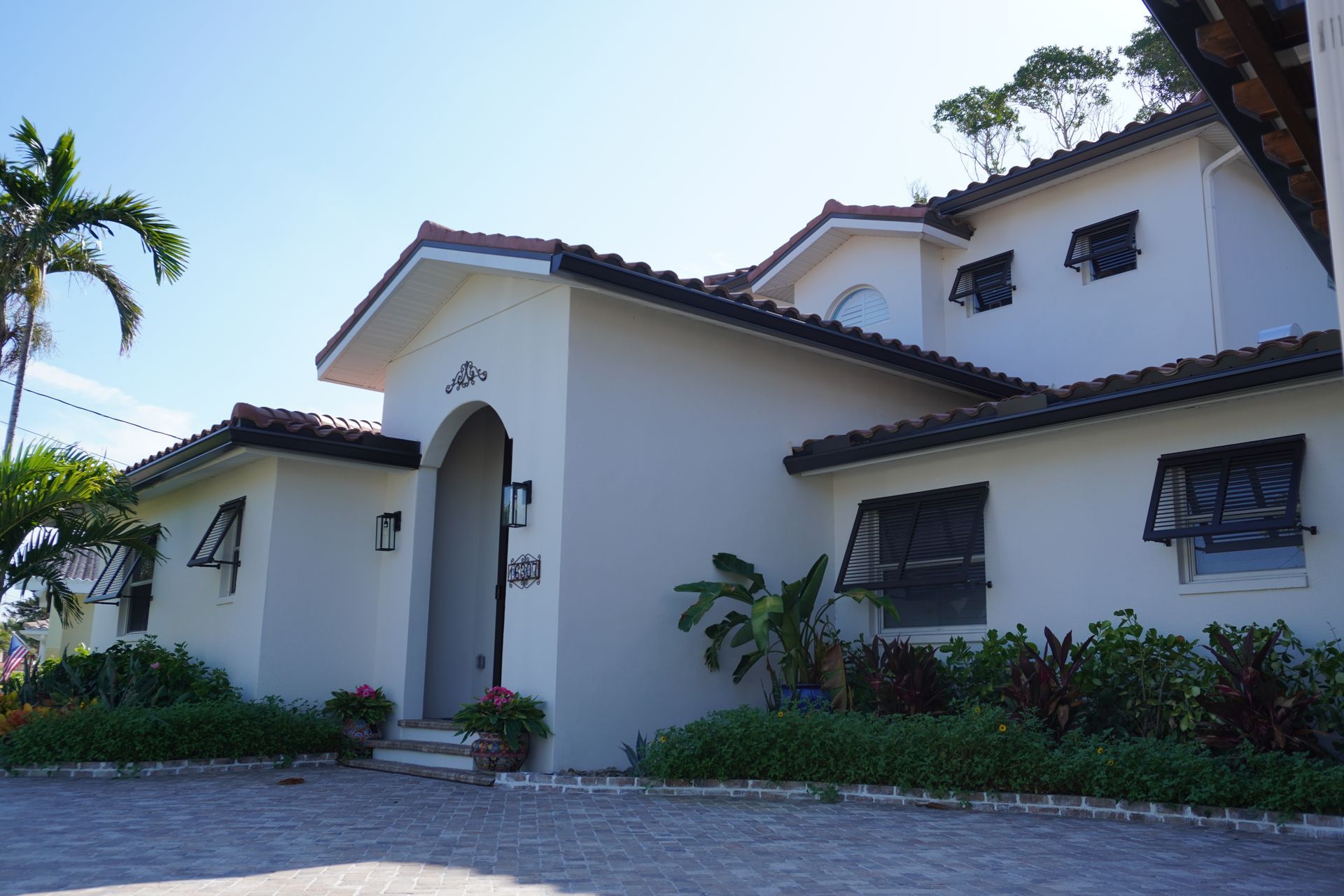 White stucco villa with red-tile roof, arched entry, and palm trees in front under a blue sky