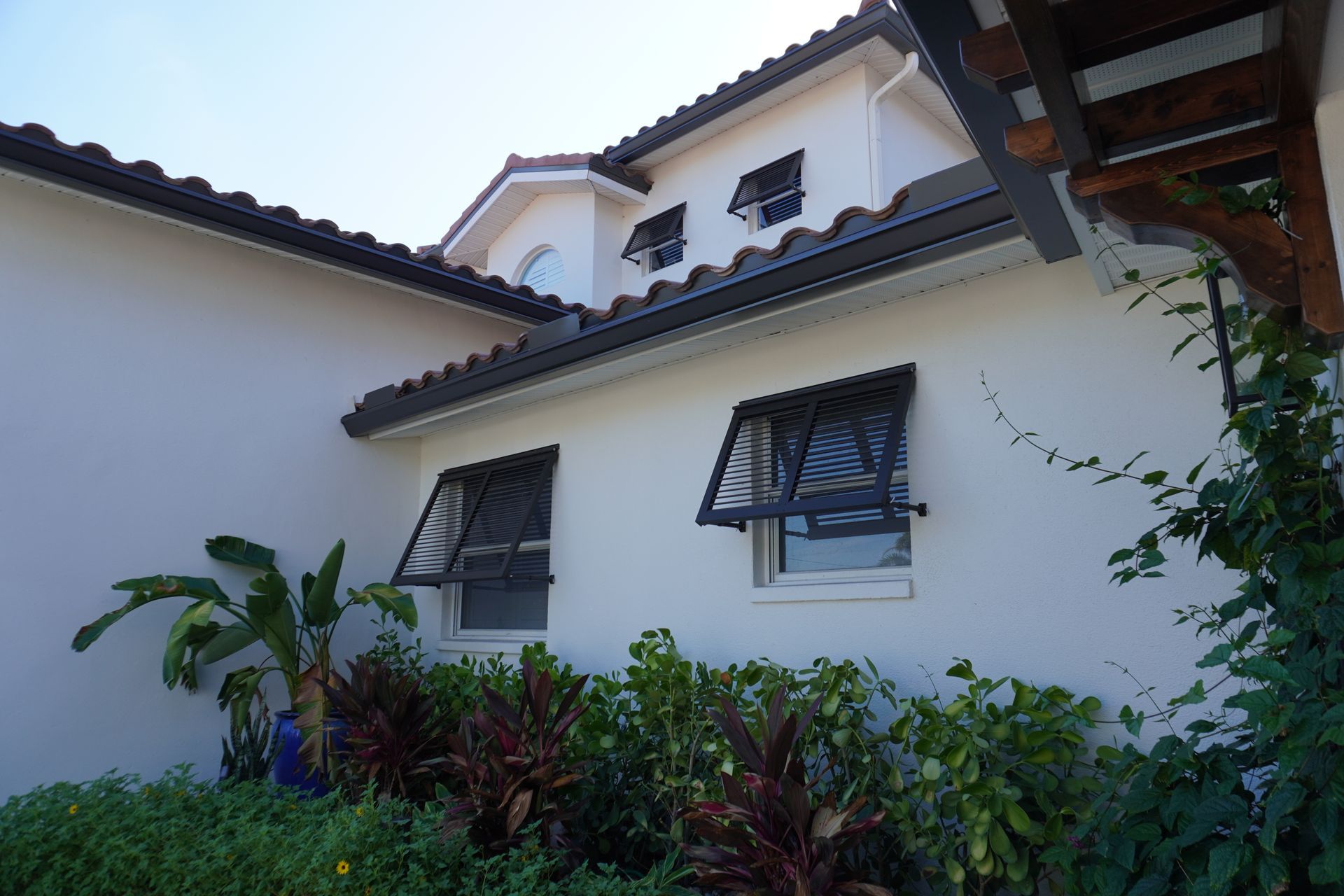 White stucco house with dark roof, windows, and lush green plants in front