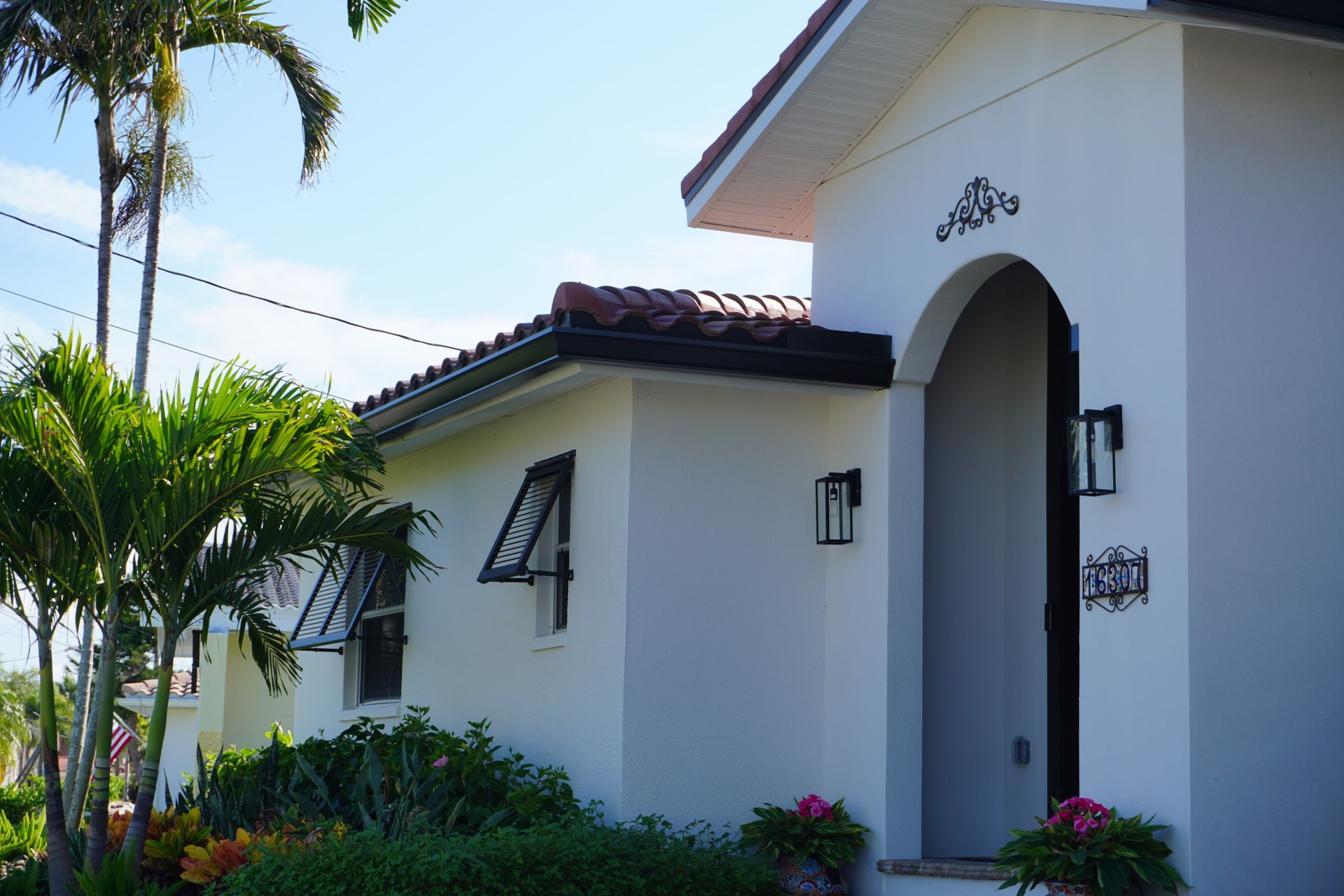 White house entrance with arched doorway, red-tiled roof, and tropical landscaping in bright sunlight